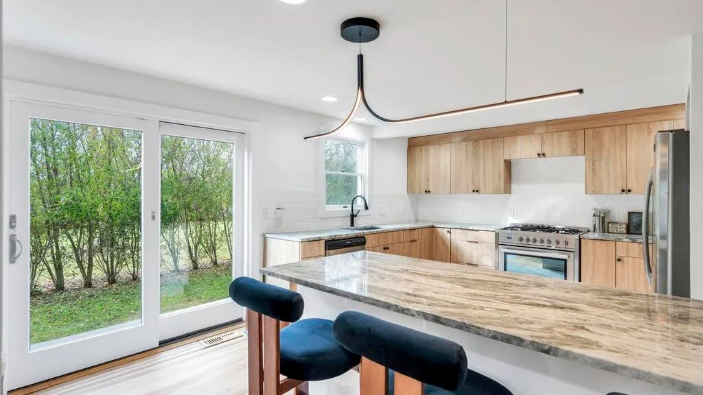 Una cocina luminosa con una isla grande y puertas de vidrio junto a la vegetación.