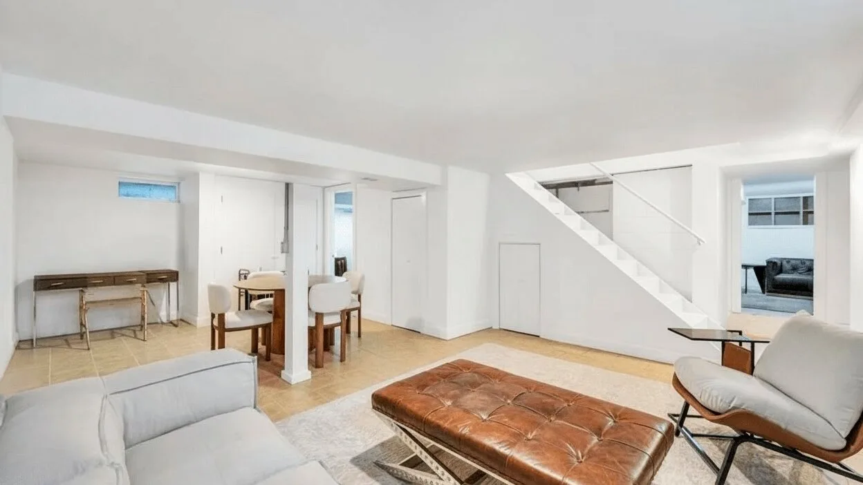 Una sala luminosa con una mesa baja marrón y asientos claros bajo una escalera.