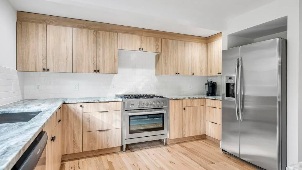 Una cocina con gabinetes de madera clara, una estufa de acero inoxidable y un refrigerador grande.