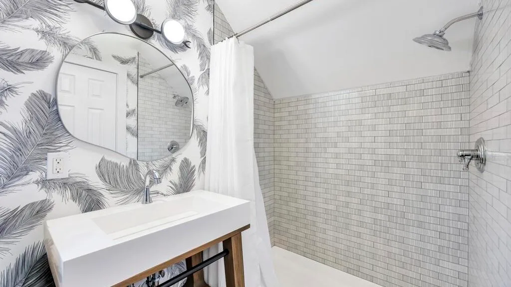 Un baño con un lavabo blanco, papel tapiz estampado y una ducha con azulejos.
