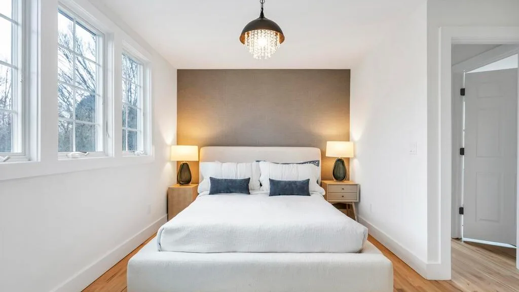 Un dormitorio luminoso con una cama tendida y ventanas altas.