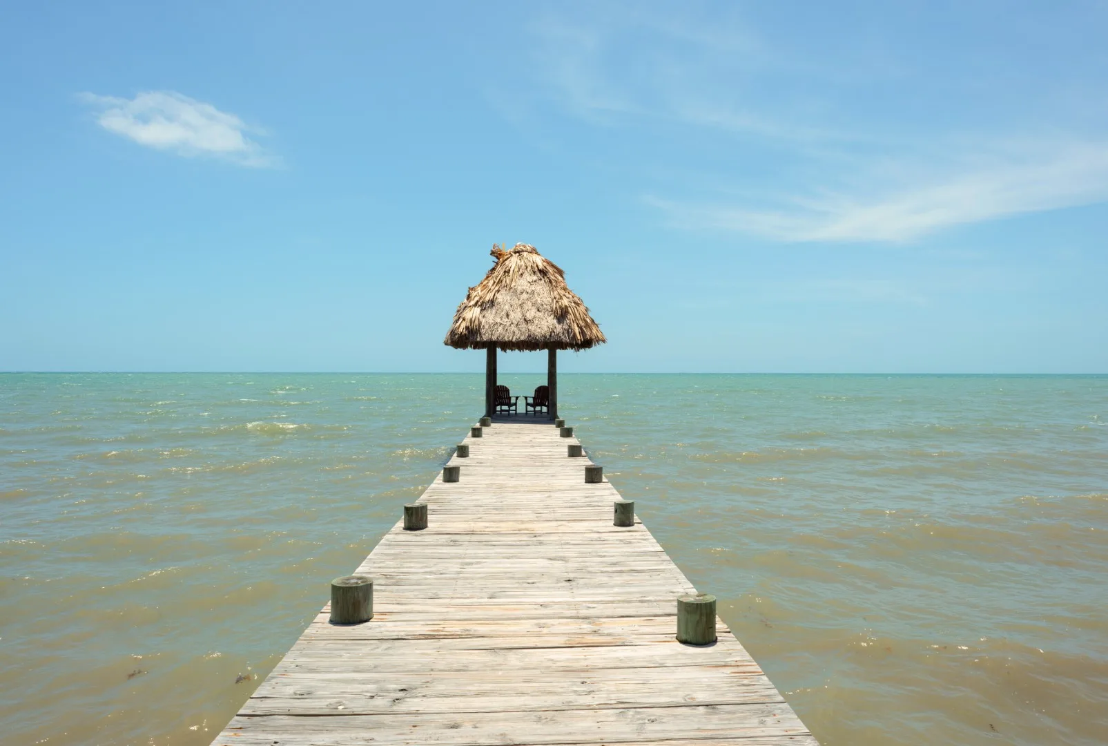 A wooden pier extends over the water toward a thatched shelter.