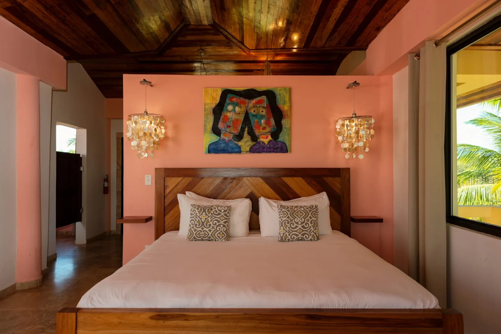 A bedroom with a bed beneath colorful wall art and hanging lights.