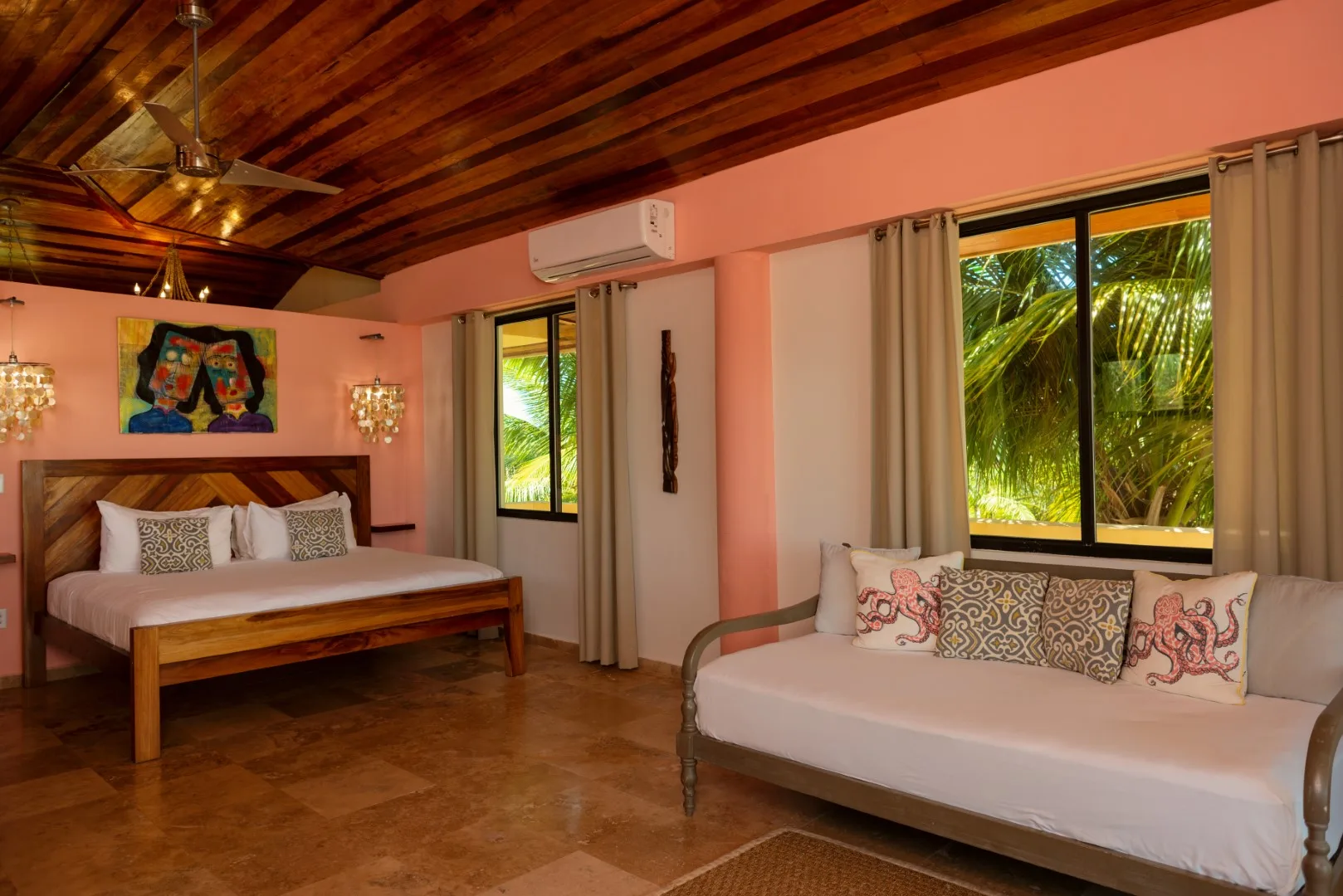 A bedroom with a bed and a cushioned seating area beside large windows.