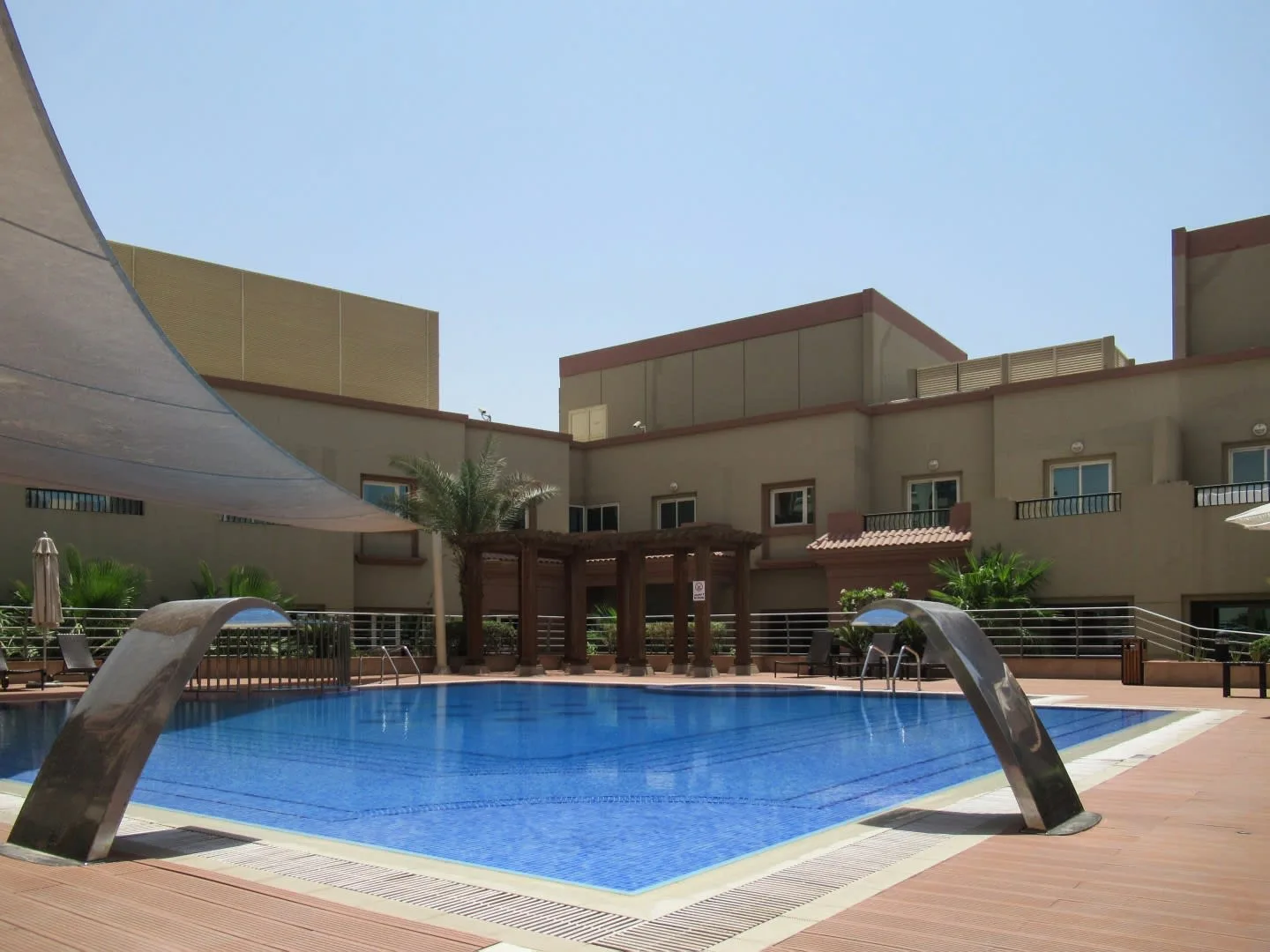 Una piscina al aire libre está junto a un edificio moderno y una zona de estar sombreada.
