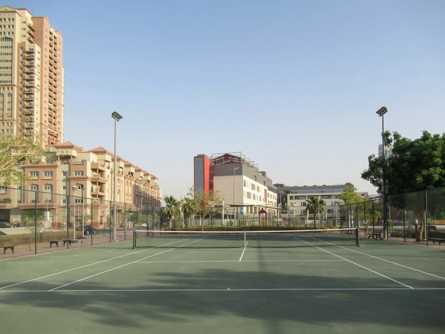 Una cancha de tenis al aire libre está frente a varios edificios.