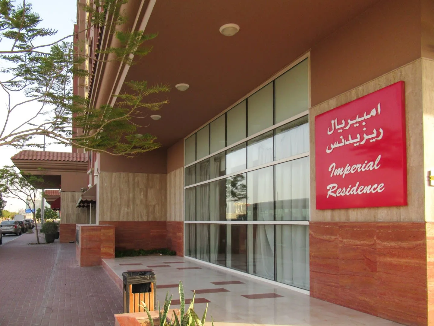 Entrada de un edificio con puertas de vidrio y un letrero rojo bajo un pasillo cubierto.