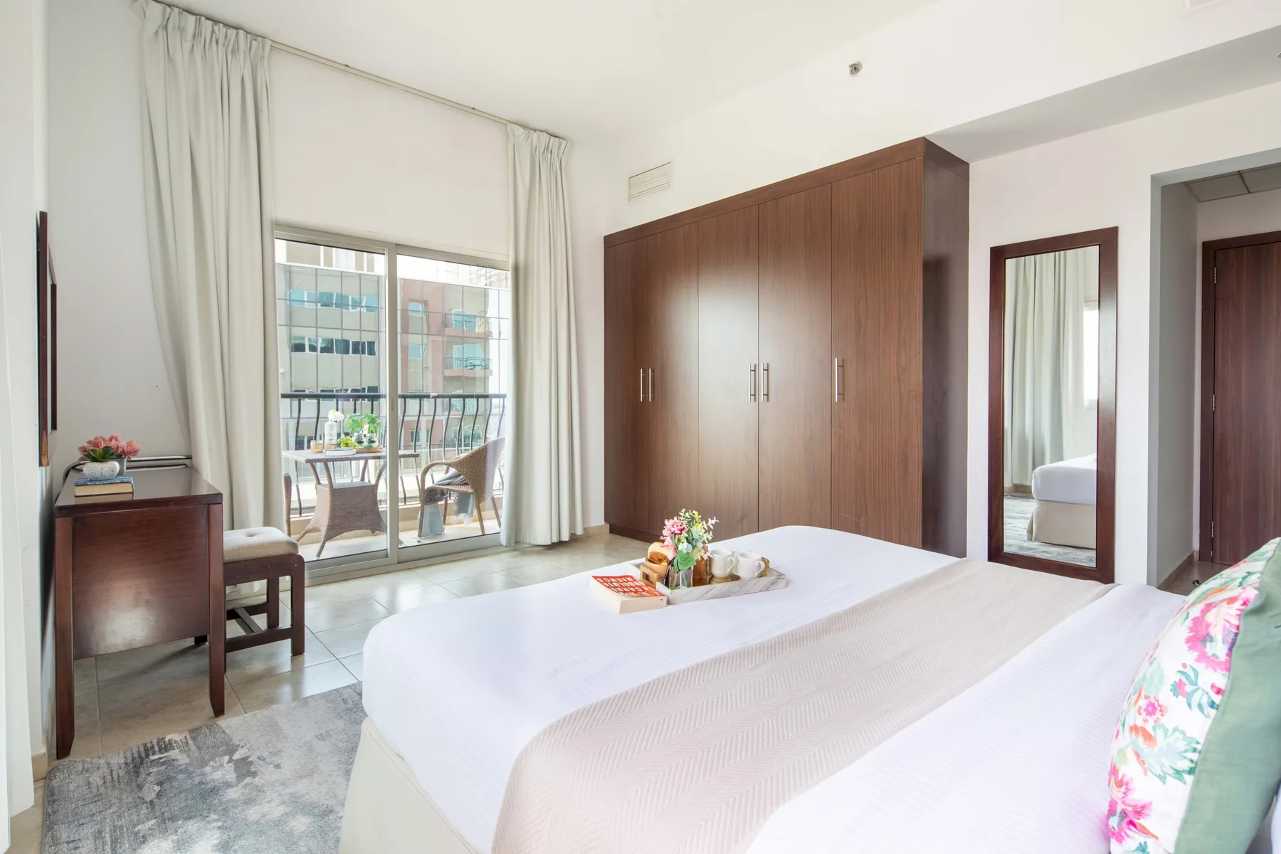 Un dormitorio luminoso con cama, armario de madera y una gran ventana con cortinas.