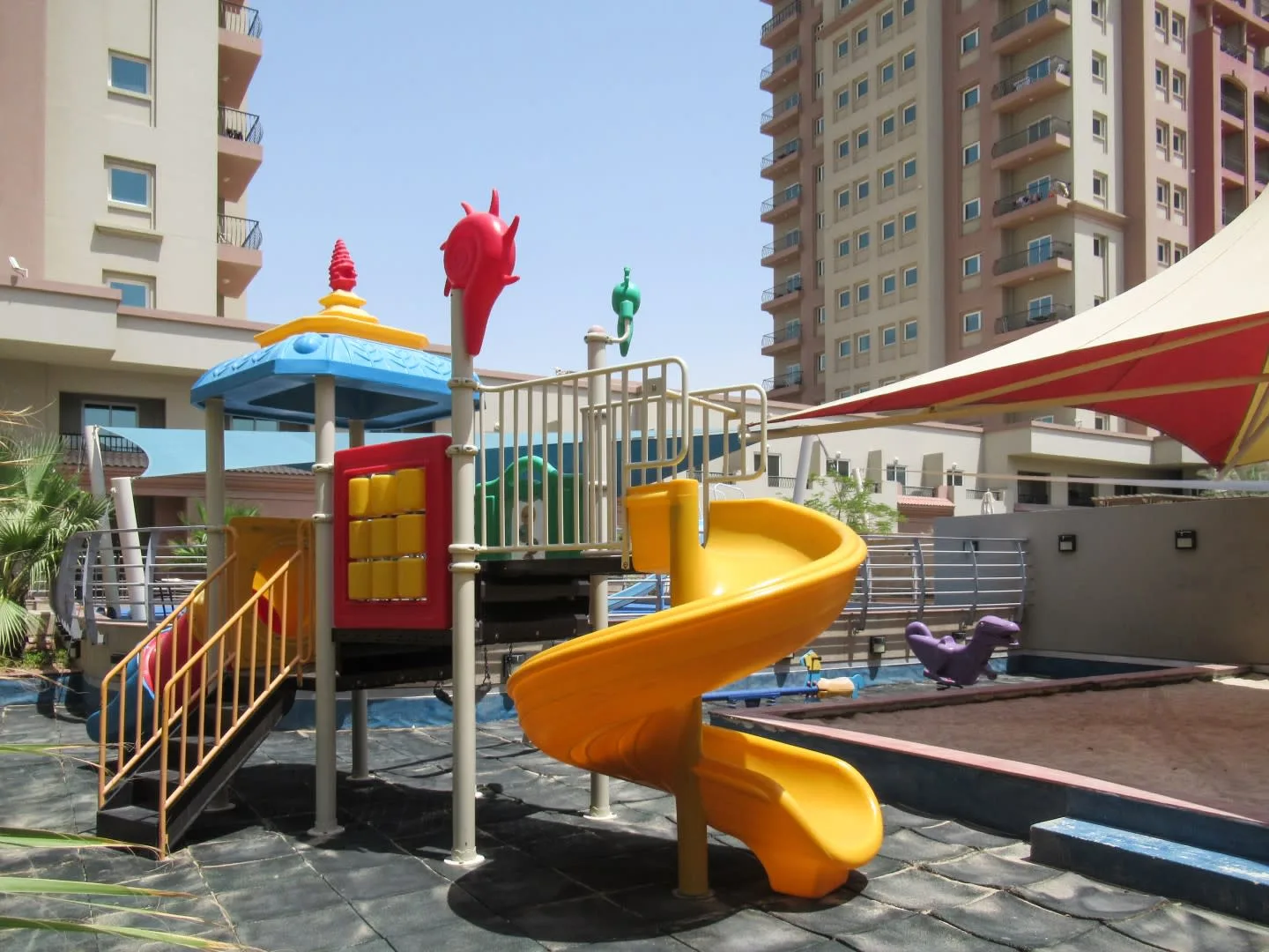 Un área de juegos al aire libre con un tobogán amarillo junto a una piscina.