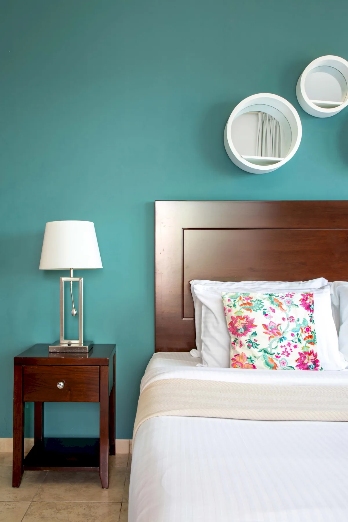 Un dormitorio con una cama de madera, ropa de cama blanca y un cojín floral.