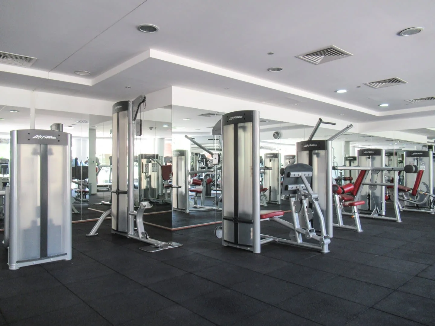 Un gimnasio con máquinas de pesas, equipos de ejercicio y suelo oscuro.