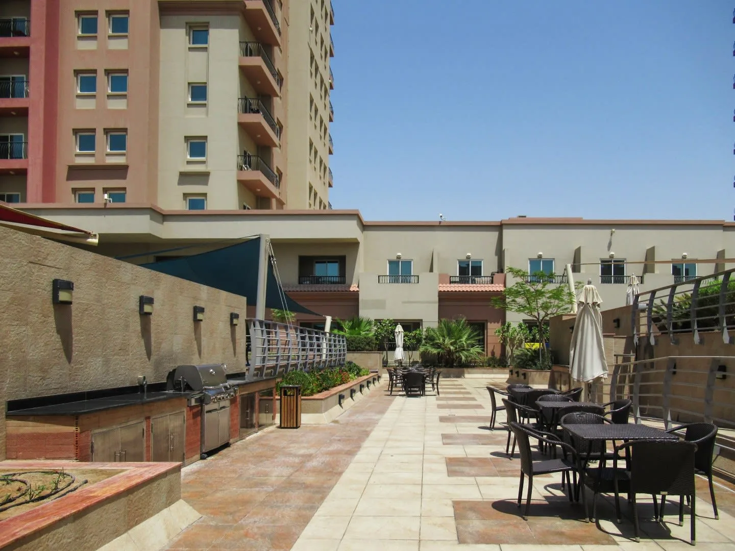 Una terraza al aire libre con mesas y sillas junto a un paseo ajardinado.