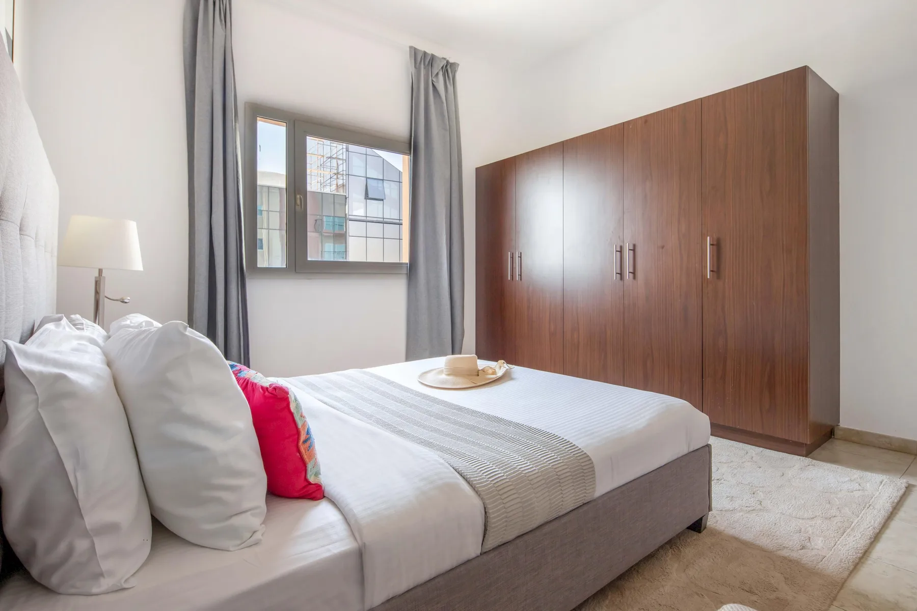 Un dormitorio luminoso con una cama junto a una ventana y un gran armario de madera.