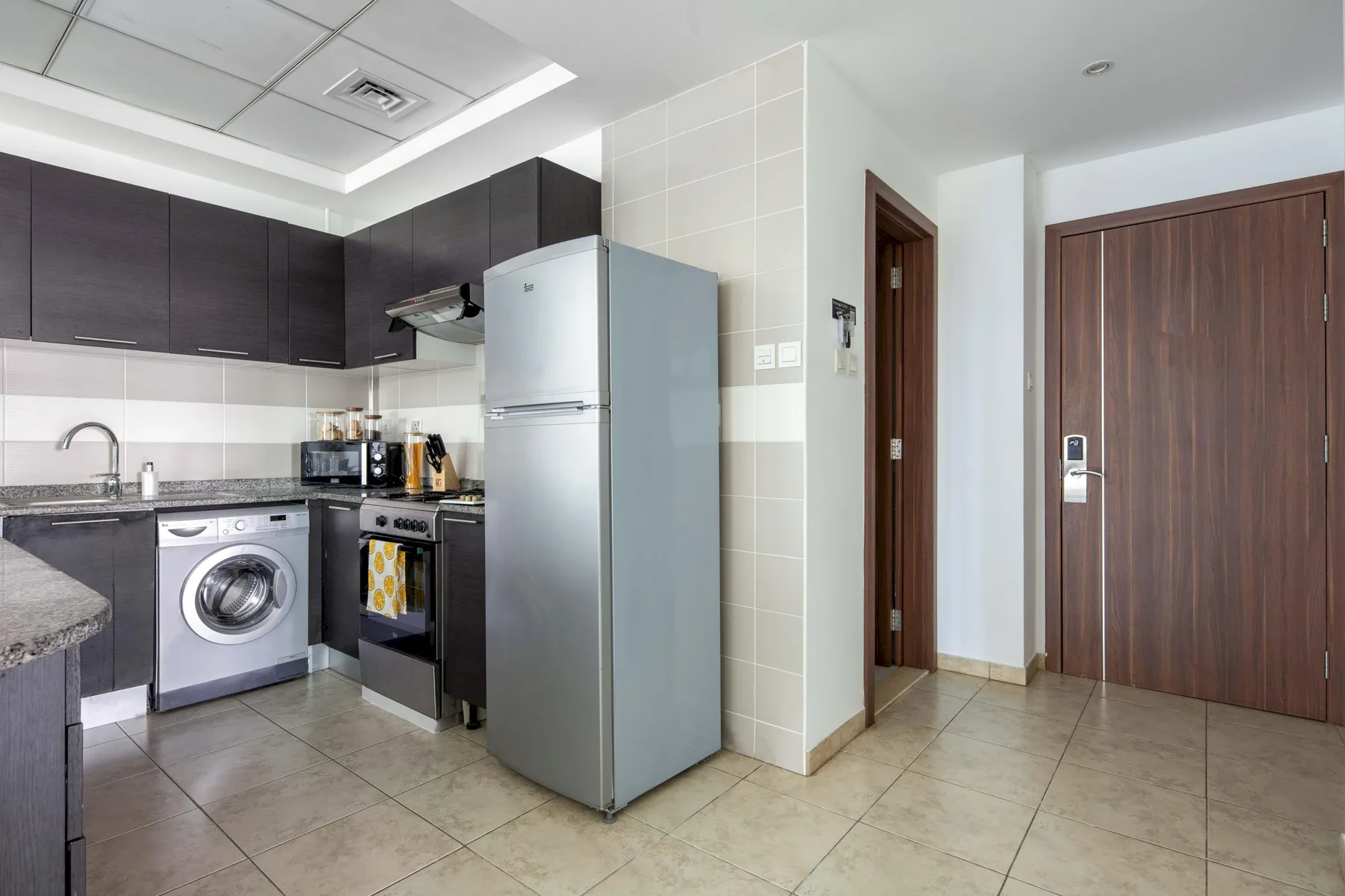 Una cocina compacta da a una zona de entrada con suelo de baldosas y puertas de madera oscura.