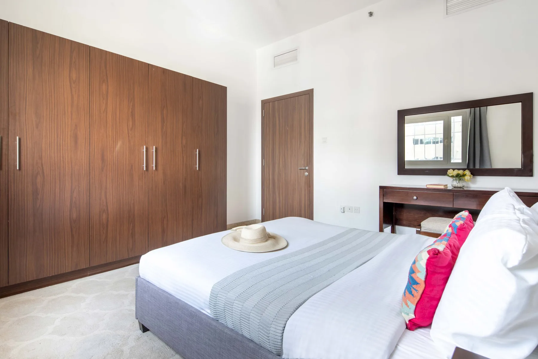 Un dormitorio con una cama tendida, un armario de madera y un escritorio.