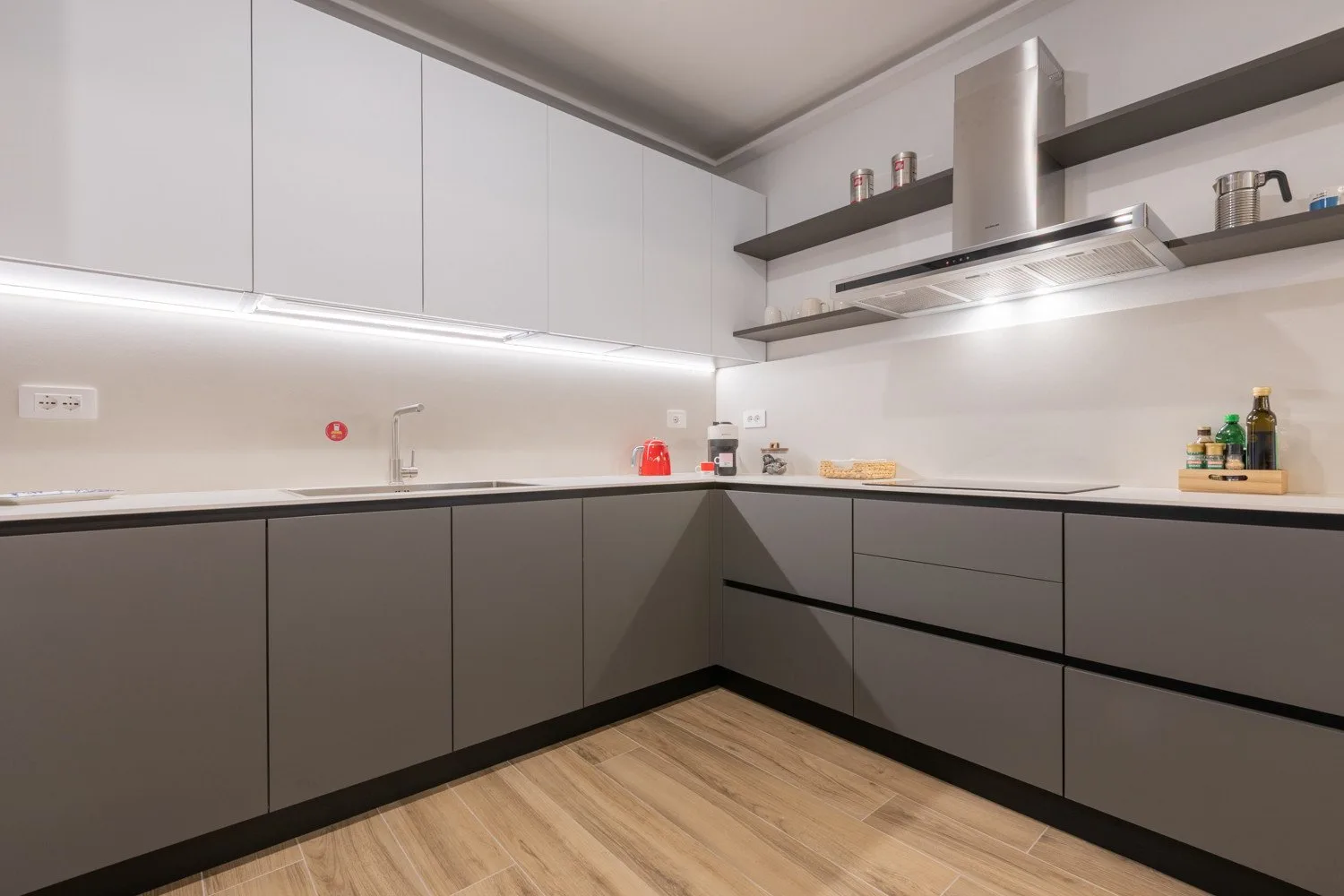 A modern kitchen with gray cabinets, white countertops, and a stainless steel range hood.