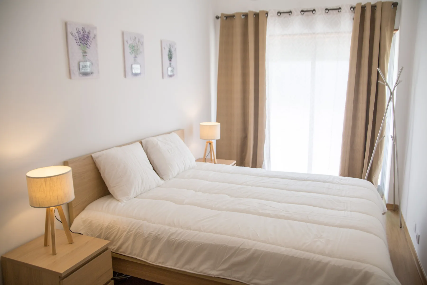 Un dormitorio luminoso con dos camas, mesillas de noche y una gran ventana con cortinas.