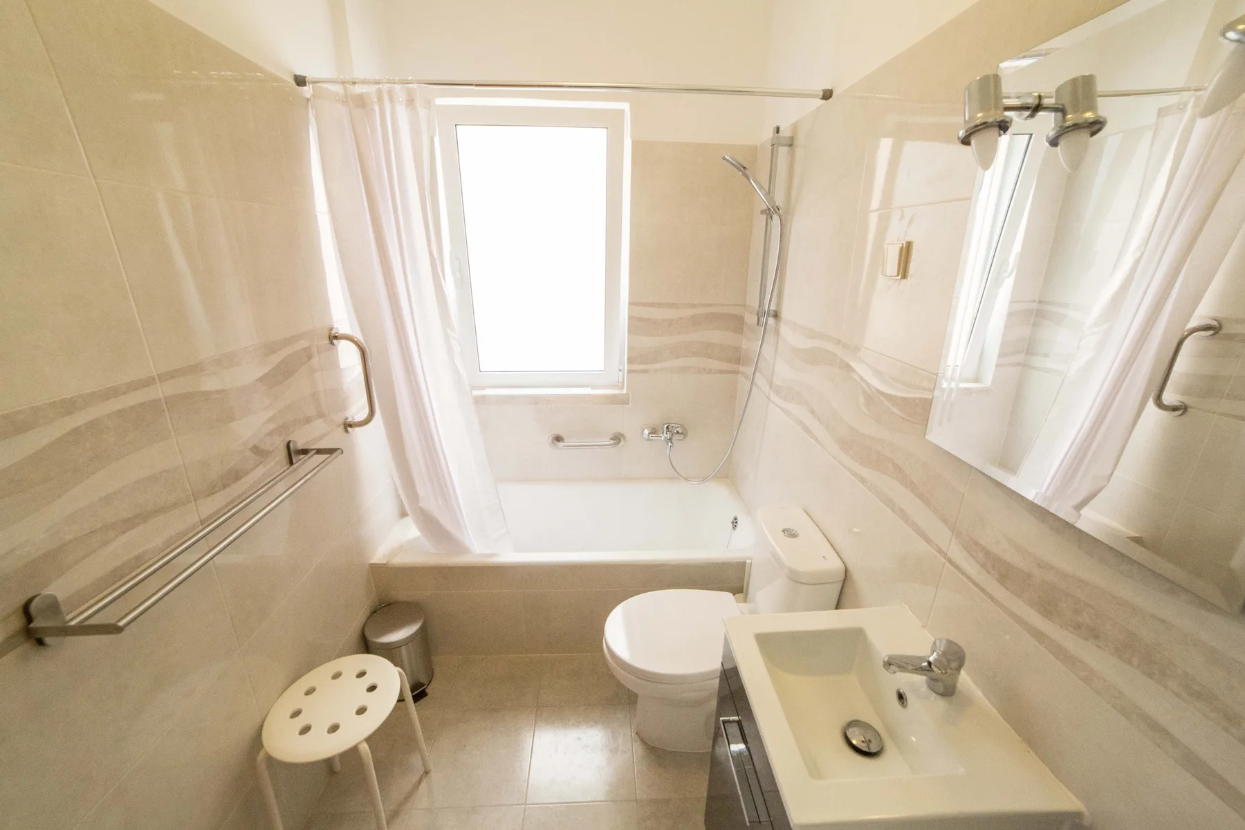 Un baño con bañera, inodoro y lavabo bajo una ventana luminosa.