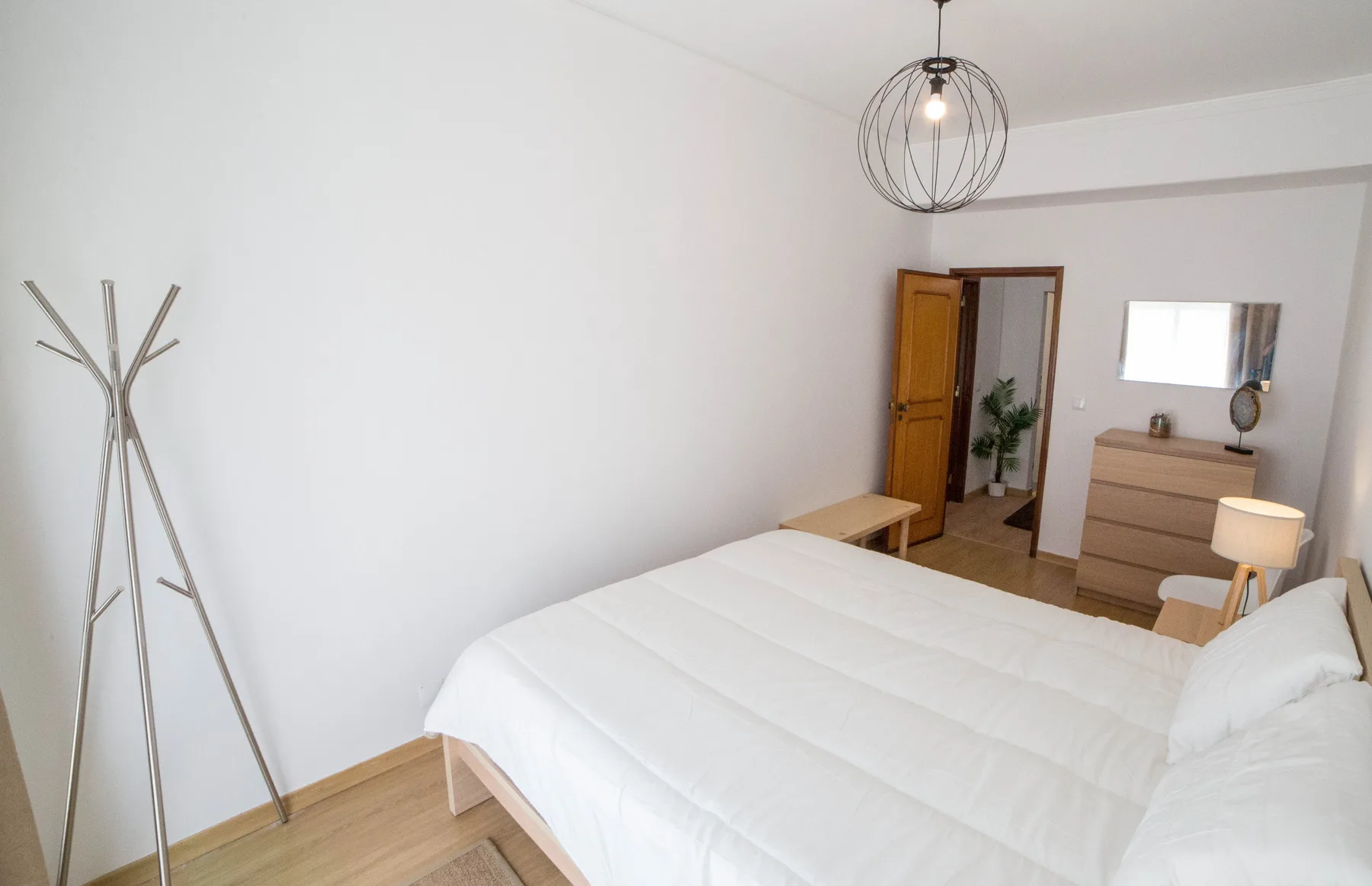 Un dormitorio luminoso con una cama grande, una cómoda y una lámpara colgante.