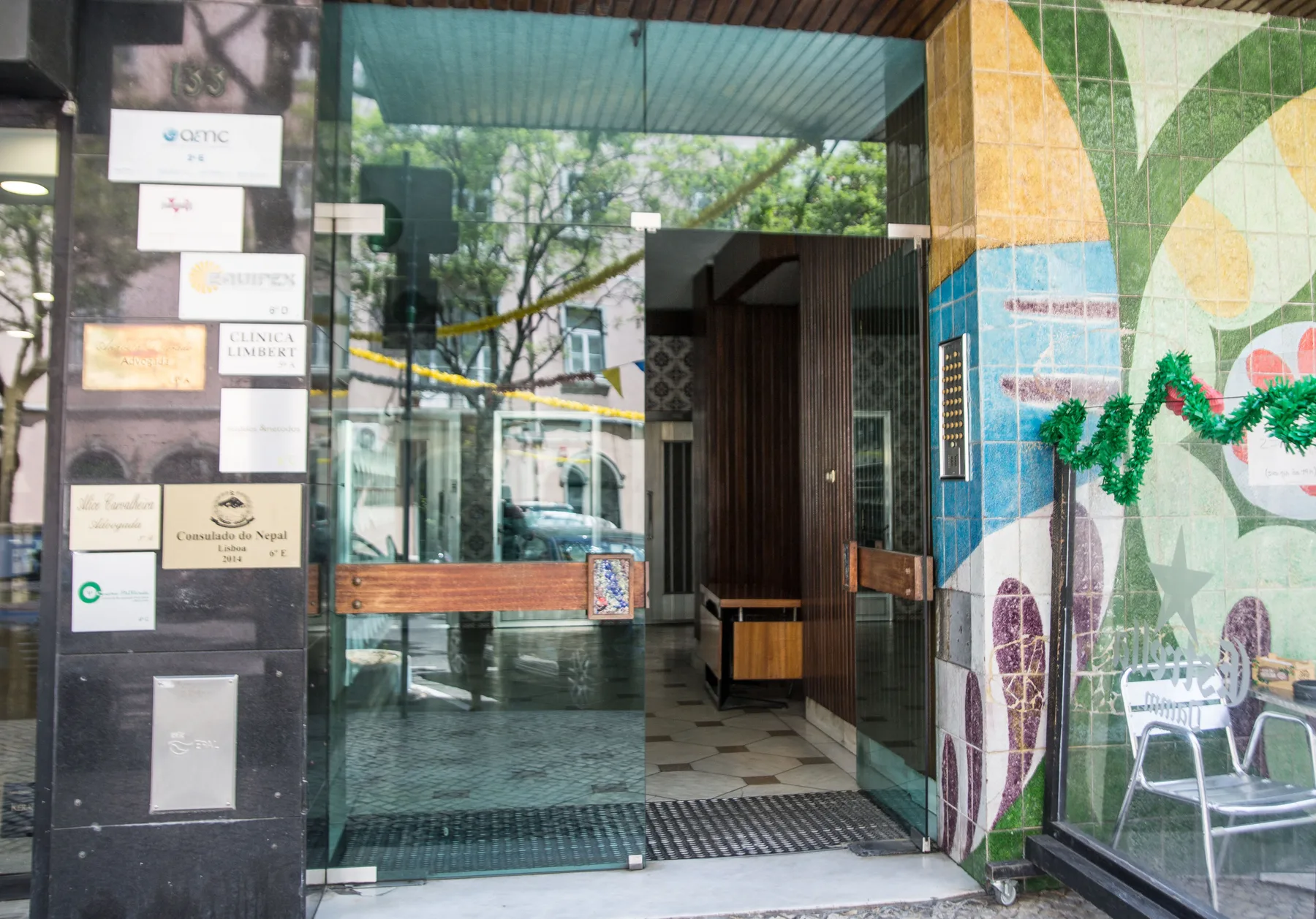 La entrada acristalada de un edificio está junto a una pared de azulejos coloridos.