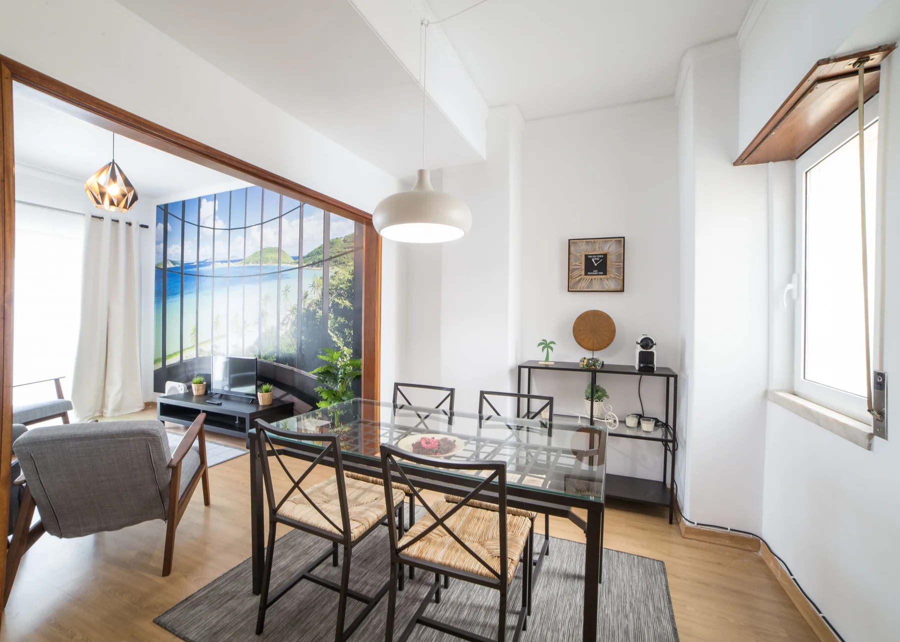 Un comedor luminoso con una mesa de vidrio y asientos junto a una sala de estar.