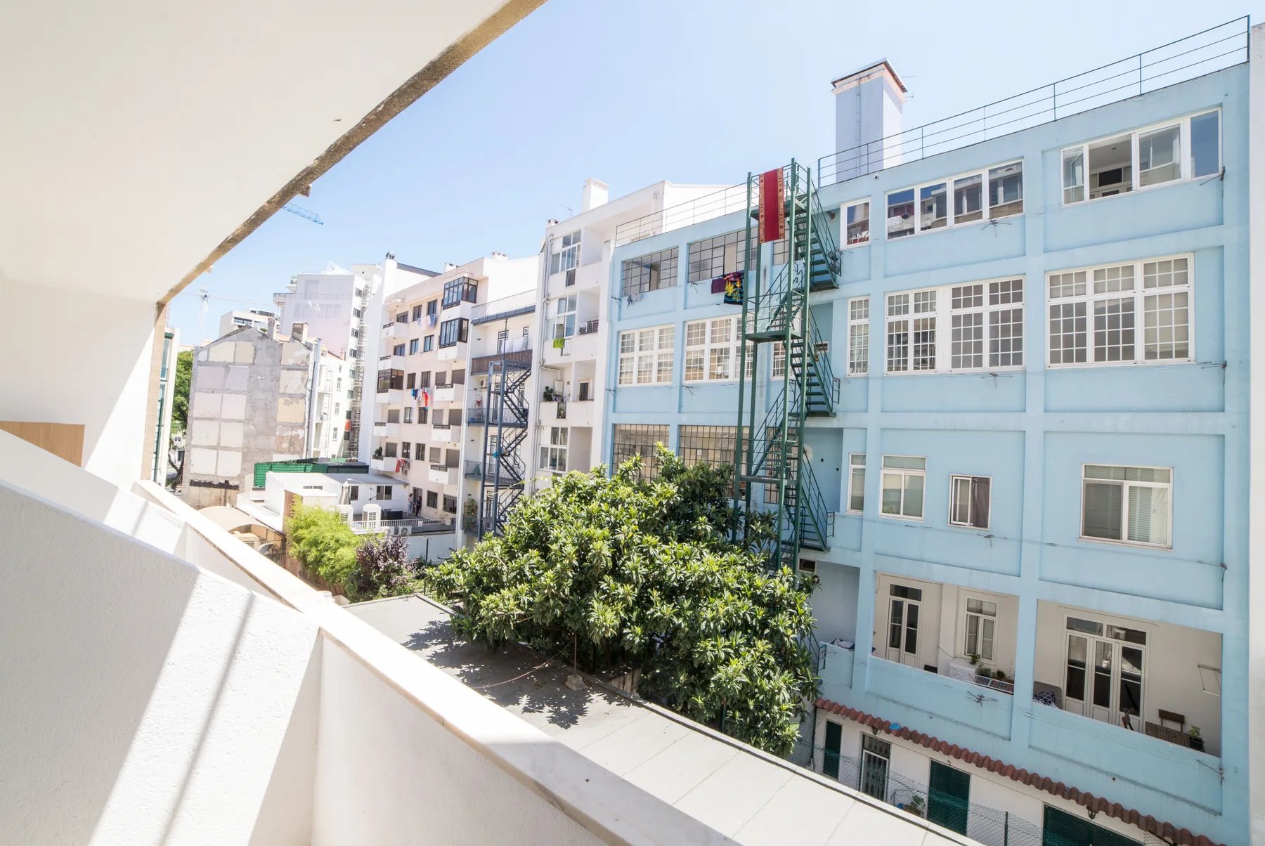 Un balcón da a edificios cercanos y árboles frondosos.