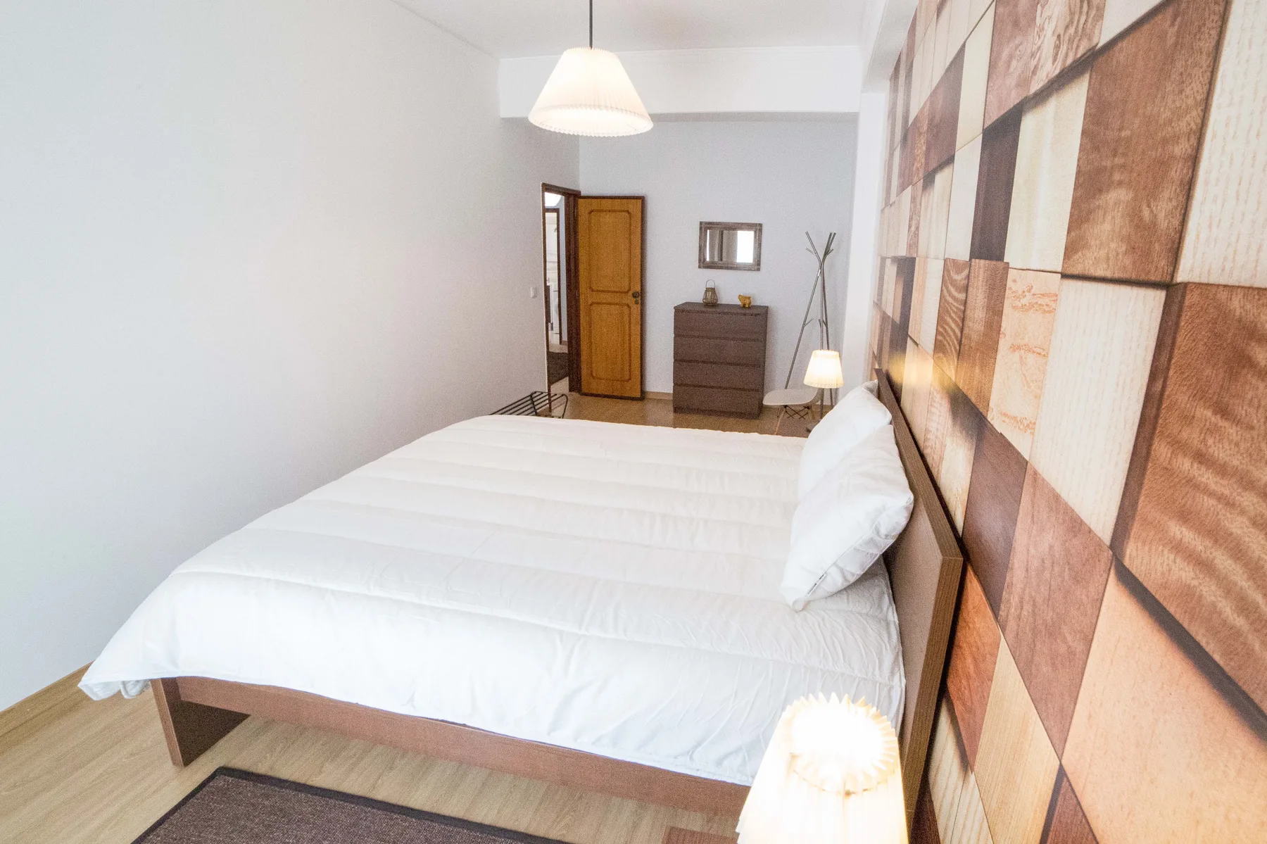 Un dormitorio con una cama bien tendida y una cómoda cerca de la puerta.