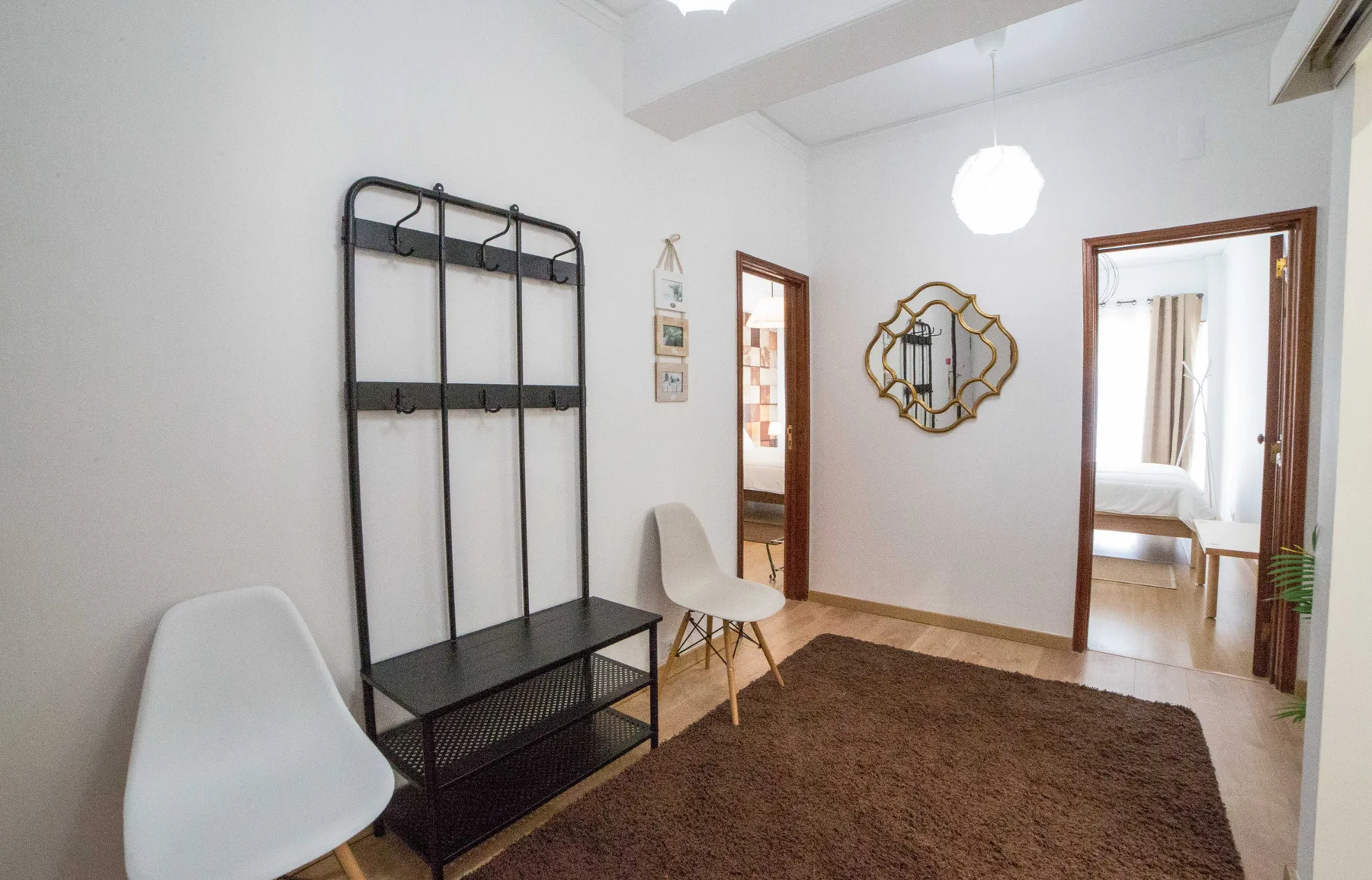 Un recibidor luminoso con una alfombra oscura, un espejo de pared y asientos.