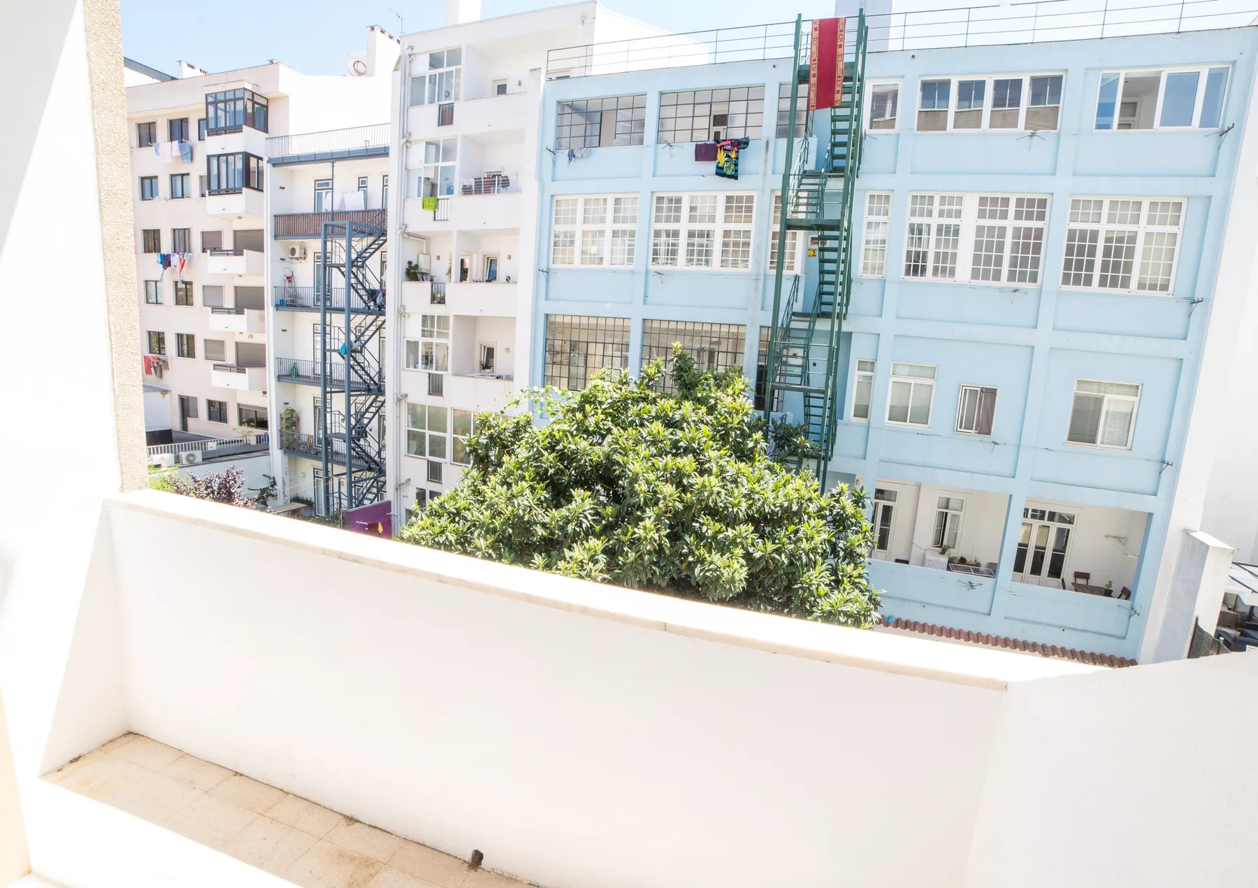 A balcony overlooks neighboring buildings and a leafy courtyard.