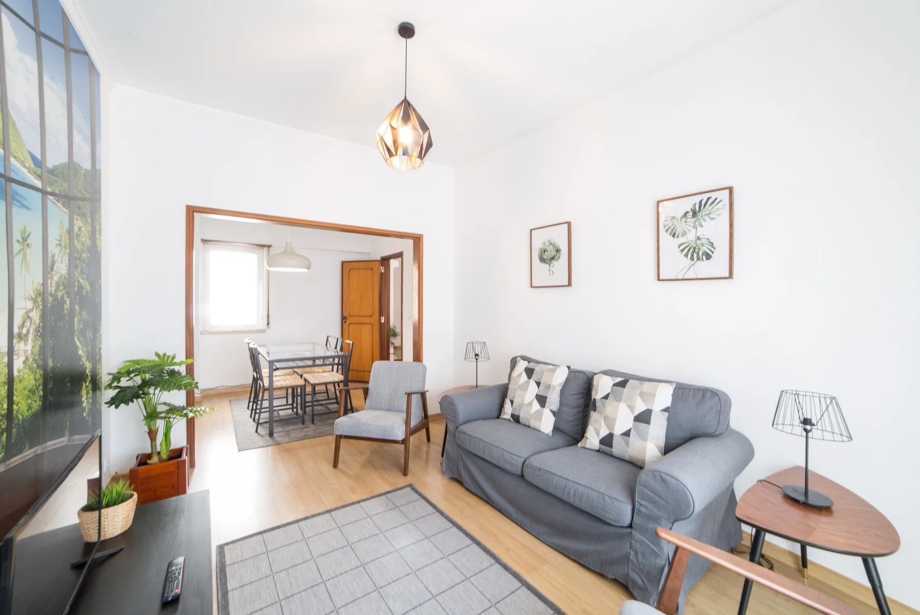 Una sala luminosa con un sofá gris y un comedor al fondo.