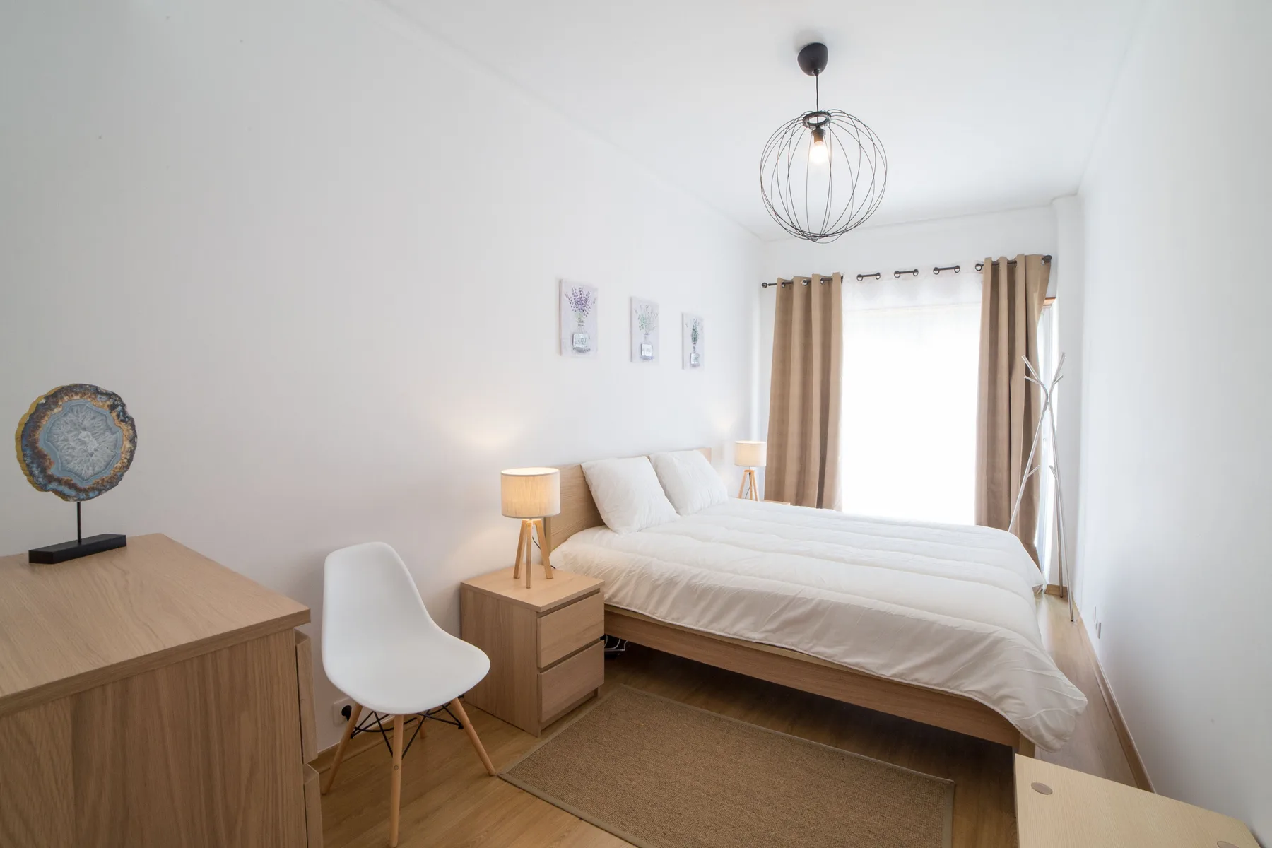 Un dormitorio luminoso con una cama, una mesita de noche y cortinas.