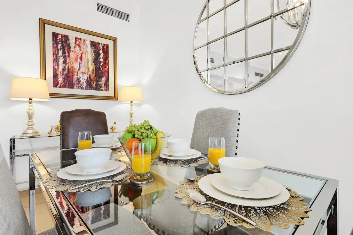 A dining area with a glass table set with dishes and fruit.