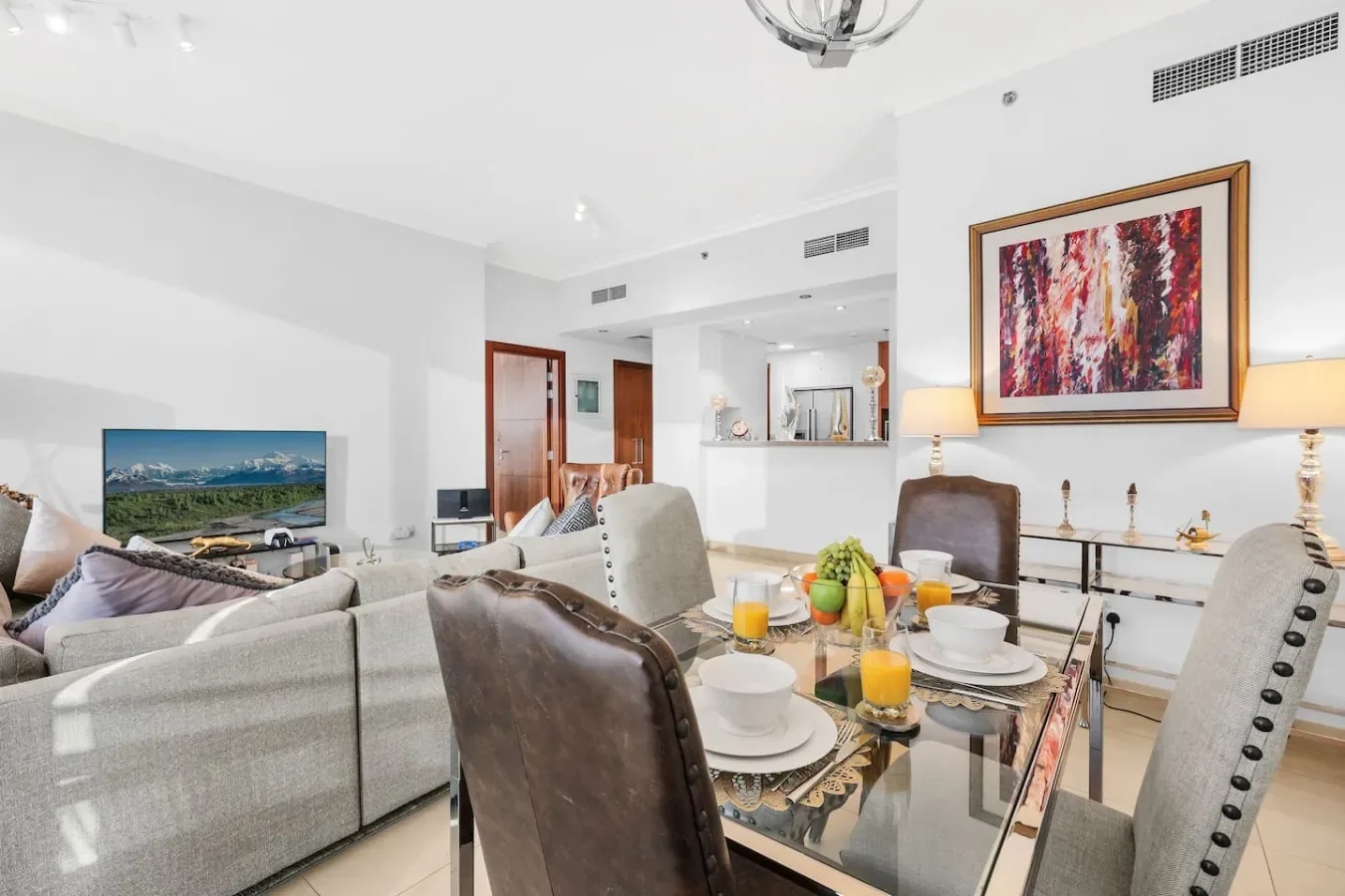 A bright living and dining area with seating, a glass table, and colorful artwork.