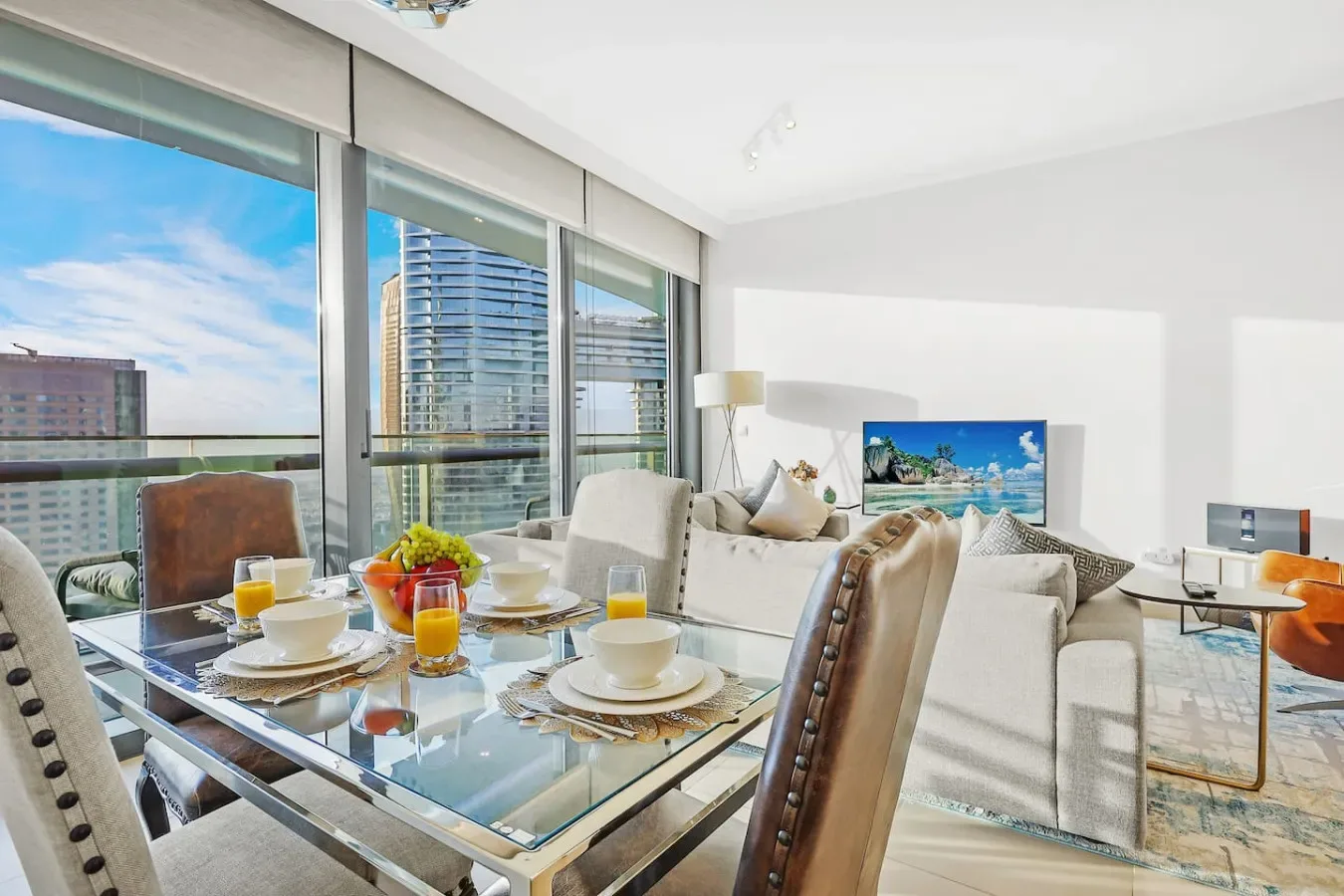 A bright living and dining area with floor-to-ceiling windows overlooking city buildings.
