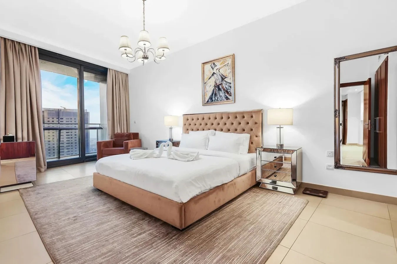 A bright bedroom with a large bed, bedside tables, and tall windows.