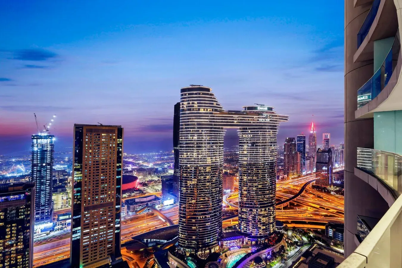 A nighttime city skyline glows beneath a blue evening sky.