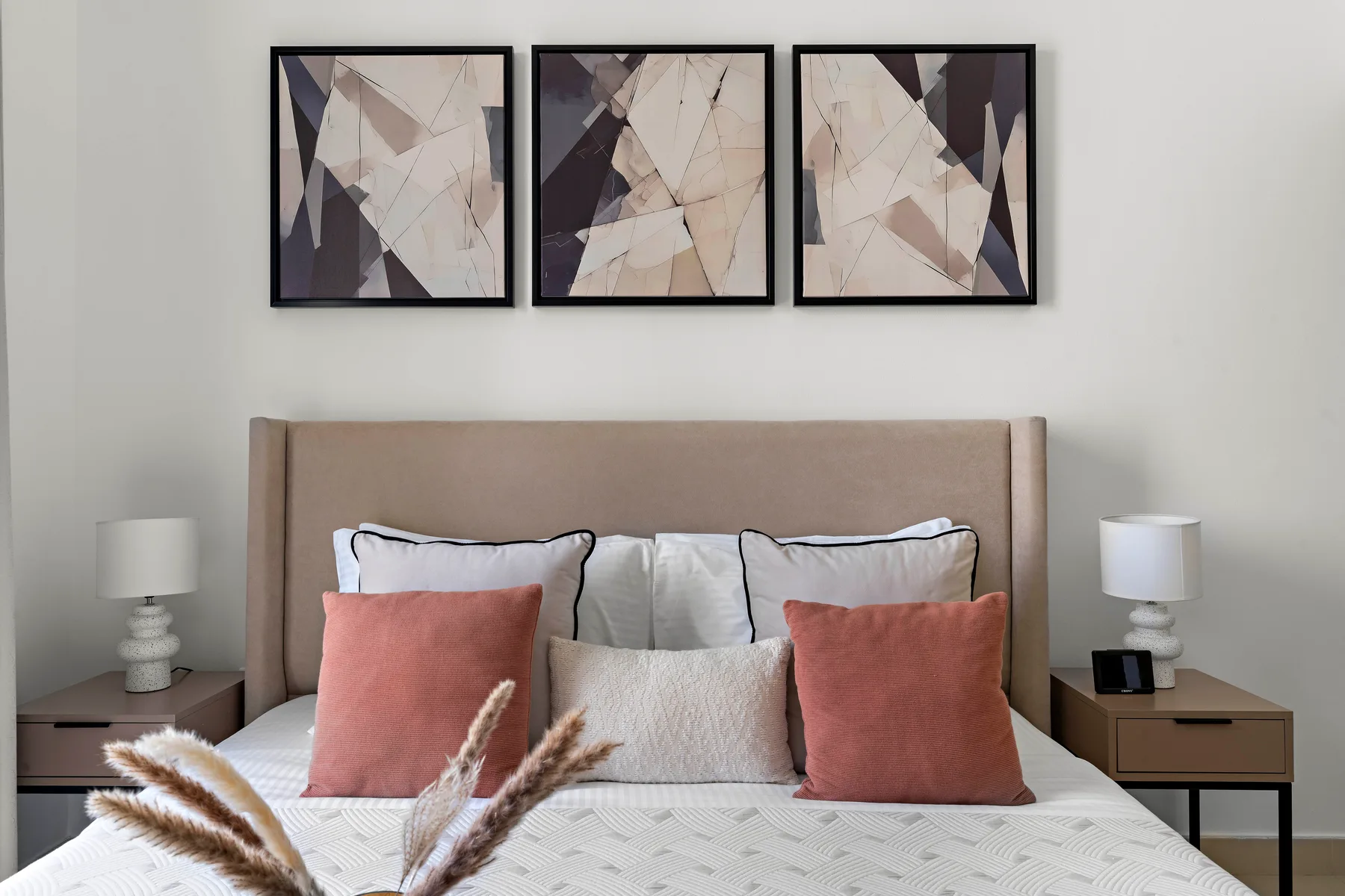 Un dormitorio con una cama, cojines decorativos y arte abstracto sobre el cabecero.