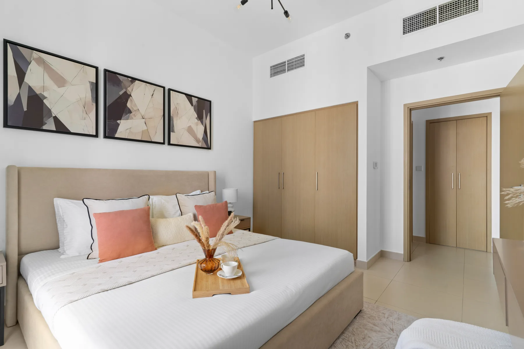 Un dormitorio con una cama bien tendida, cuadros enmarcados y armarios de madera clara.