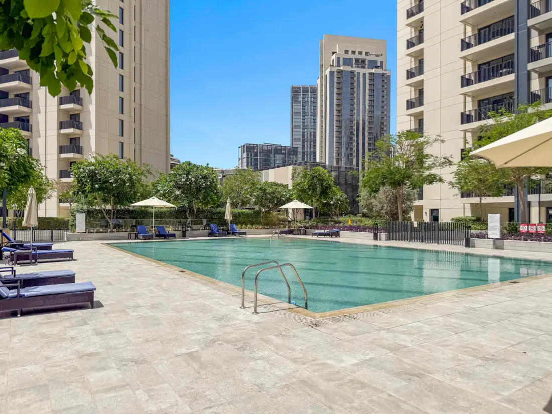Una piscina al aire libre está rodeada de edificios de apartamentos y asientos junto a la terraza.