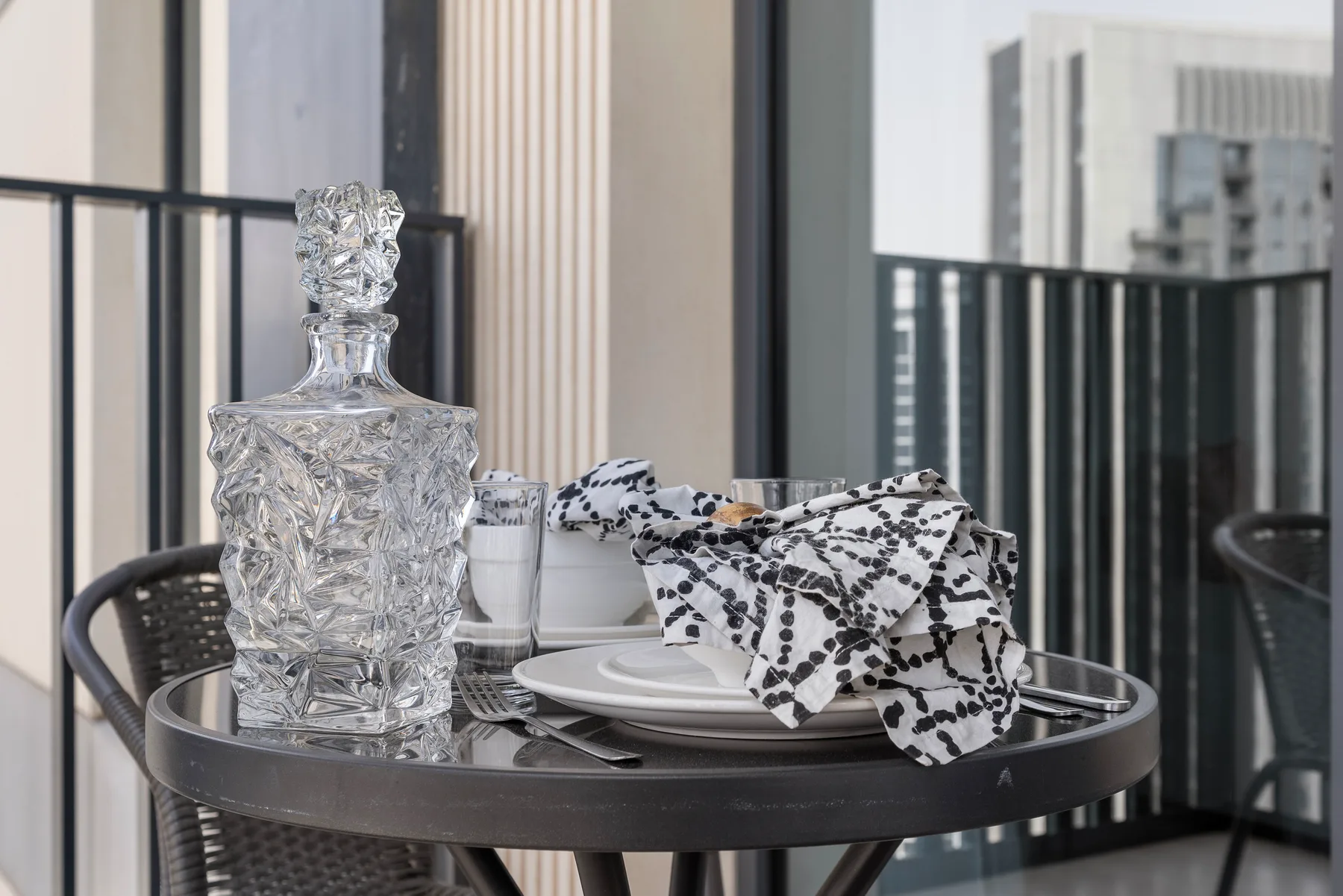 Una mesa pequeña está puesta con platos y un paño estampado junto a una barandilla de balcón.