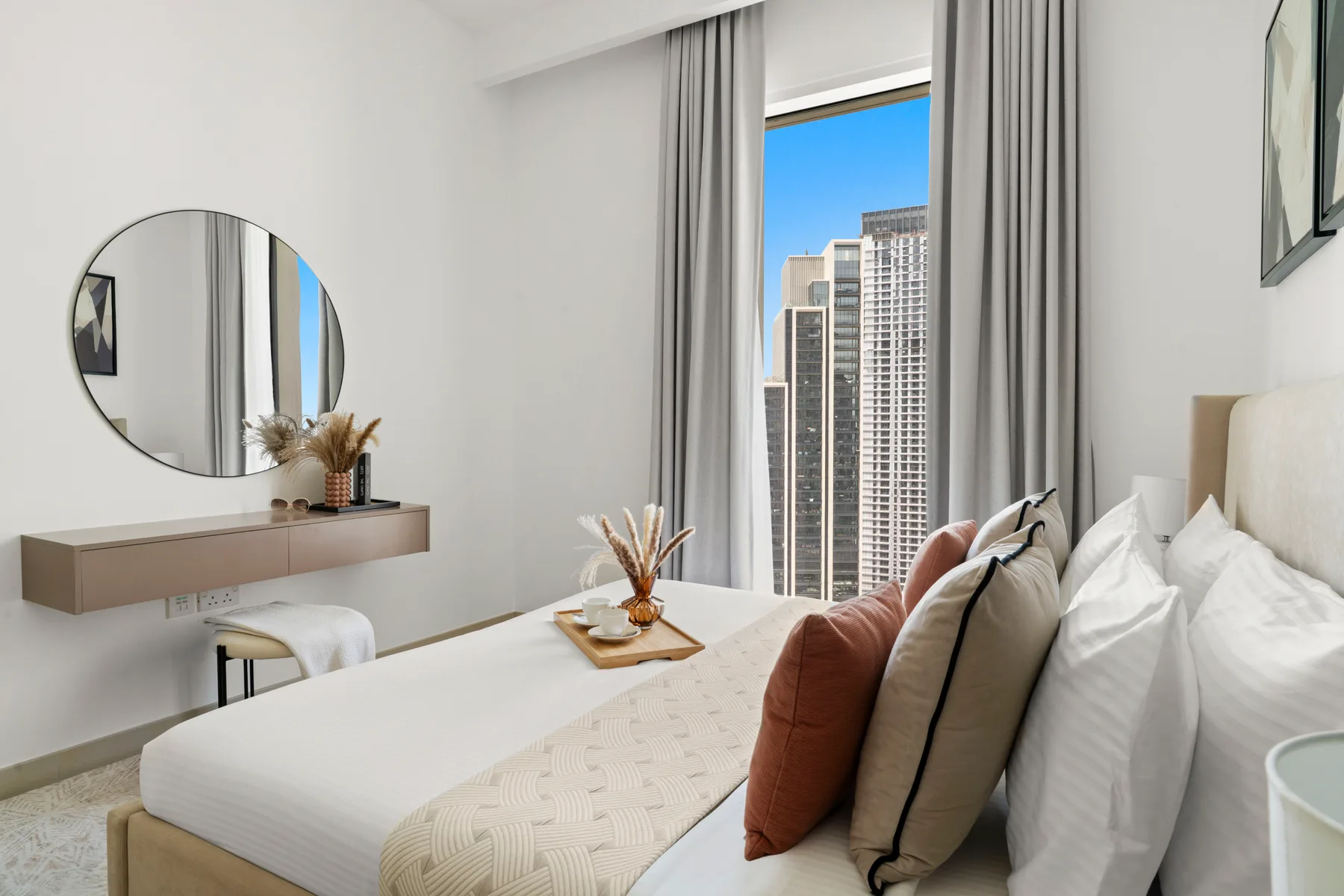 Un dormitorio con una cama bien tendida, almohadas y una vista de la ciudad por la ventana.