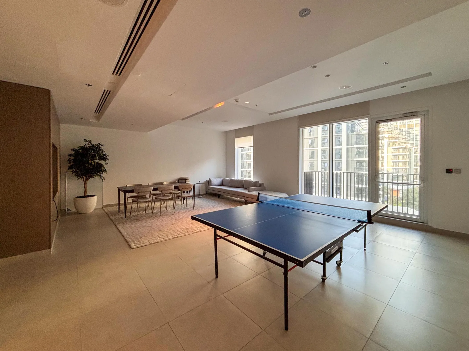Un salón luminoso cuenta con una mesa de ping-pong, una mesa de comedor y grandes ventanas.