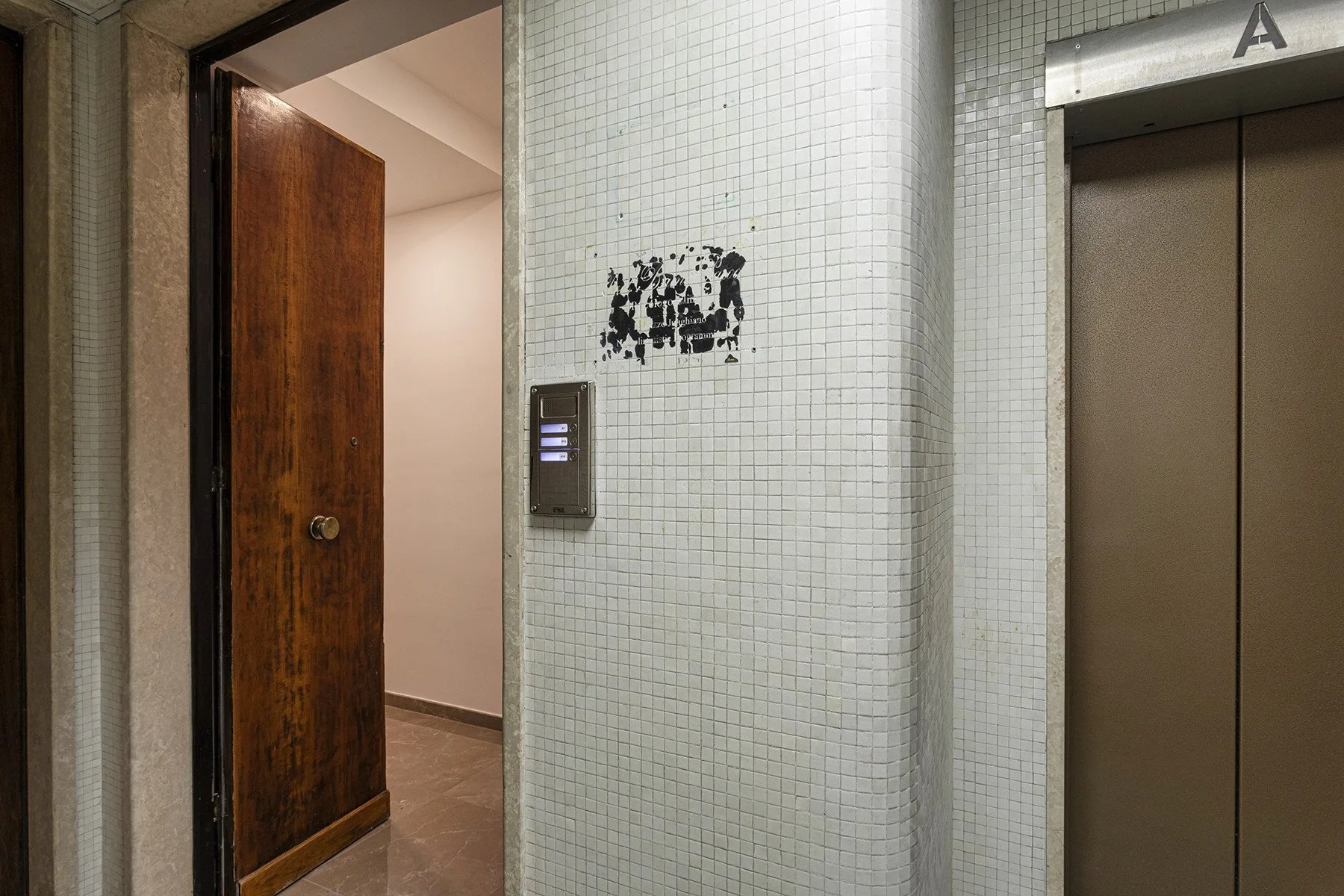 A tiled elevator lobby with an open wooden door beside the elevator.