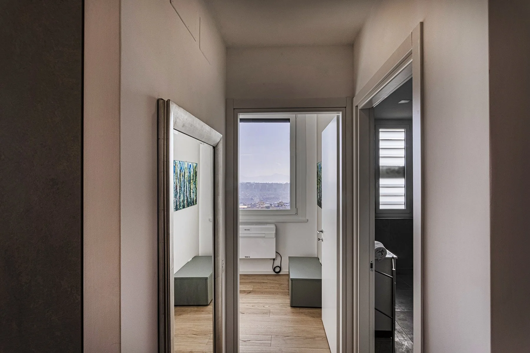 A hallway opens toward a bright room with a window and light wood flooring.