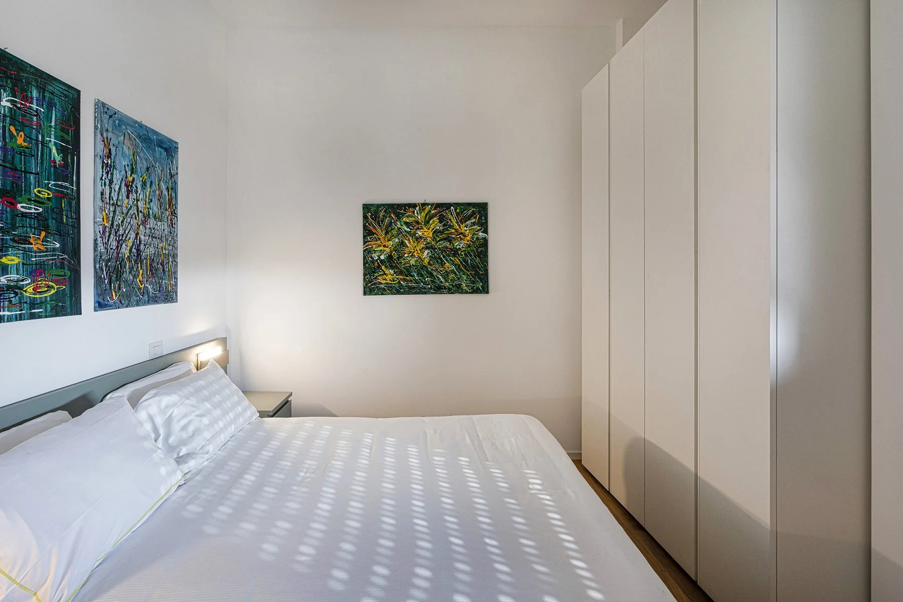 A bedroom with a bed, wall art, and tall wardrobes.
