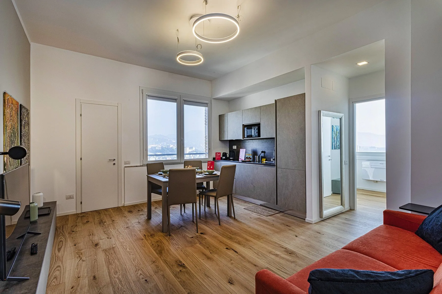 A bright open-plan room with a dining table, kitchenette, and red sofa.