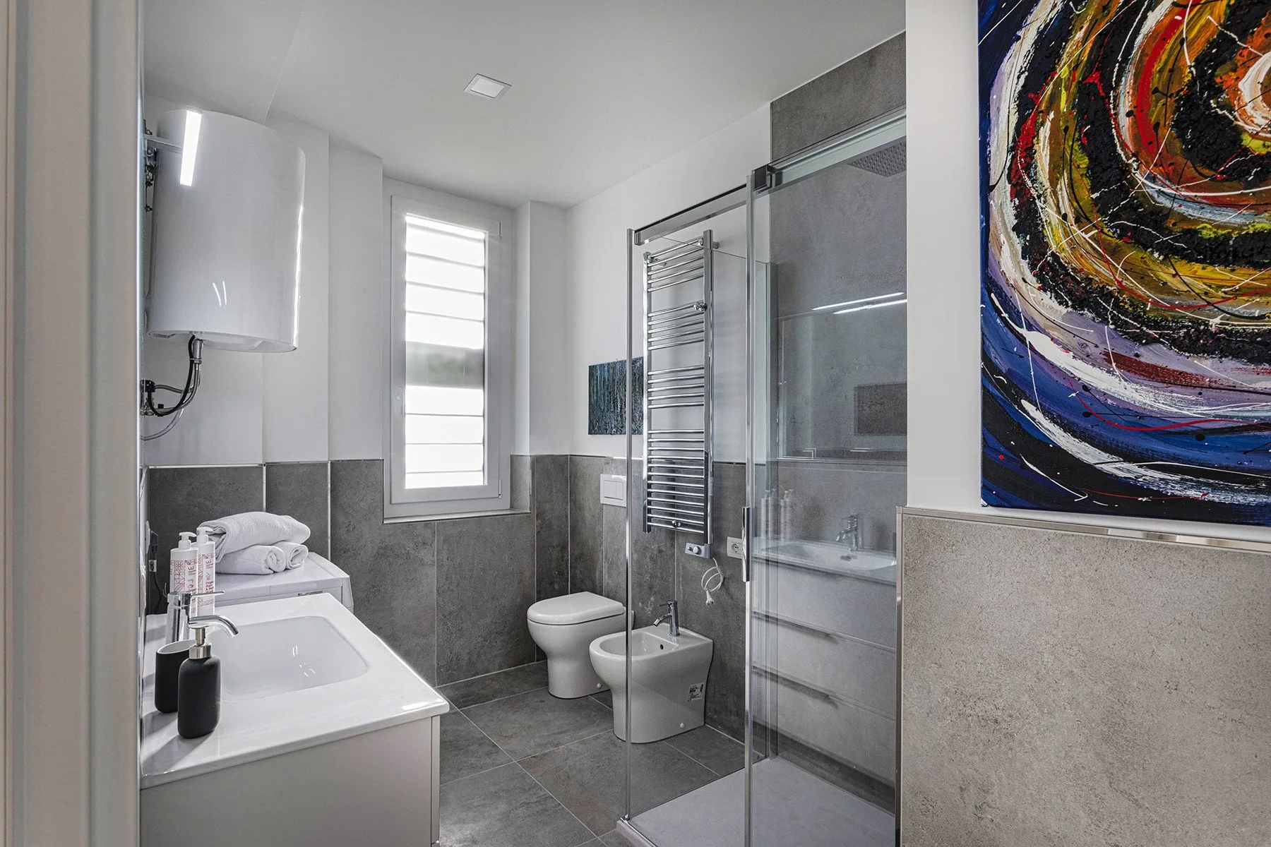 A bright bathroom with a shower, sink, toilet, and window.