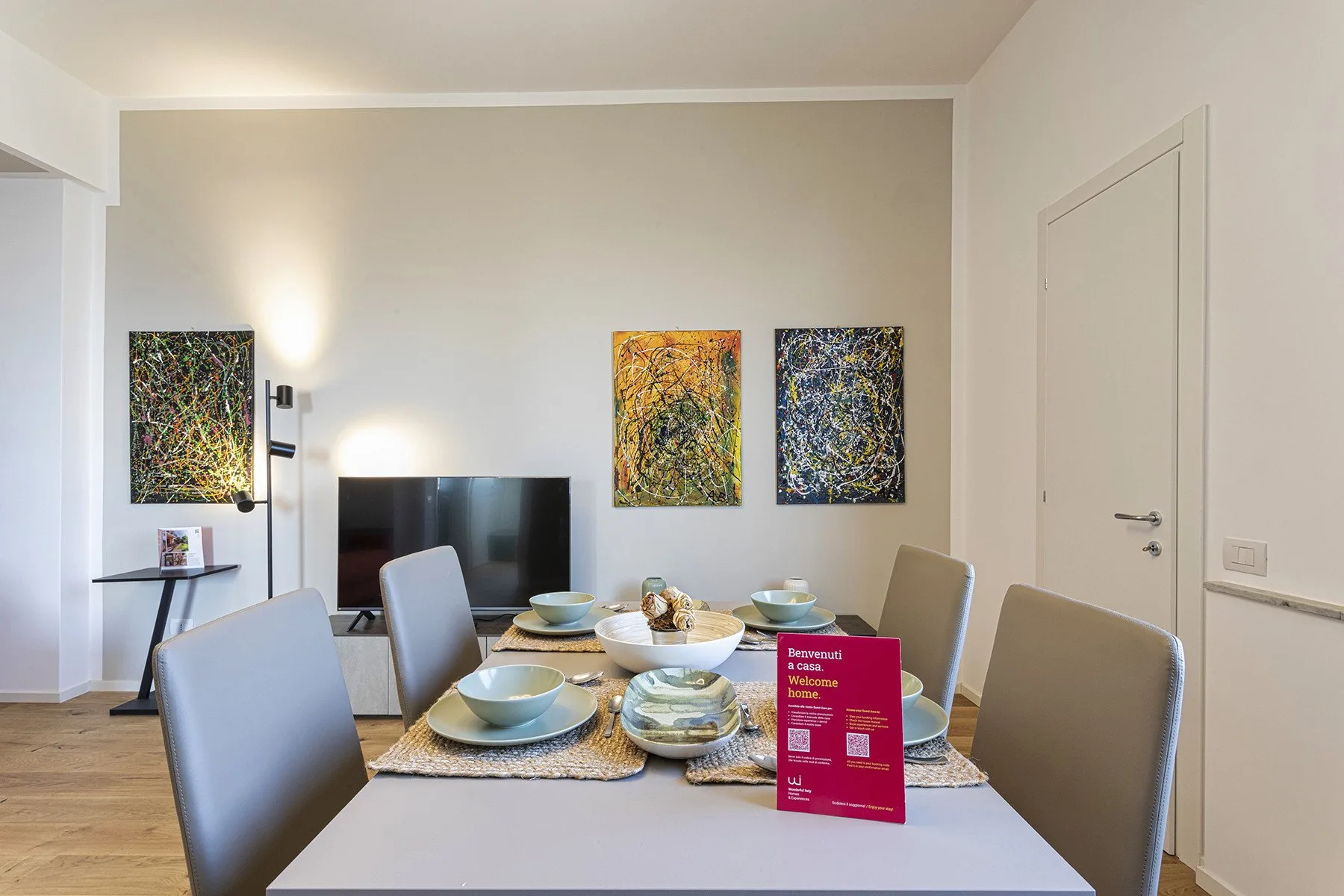 A dining area with a set table, television, and colorful artwork on the wall.