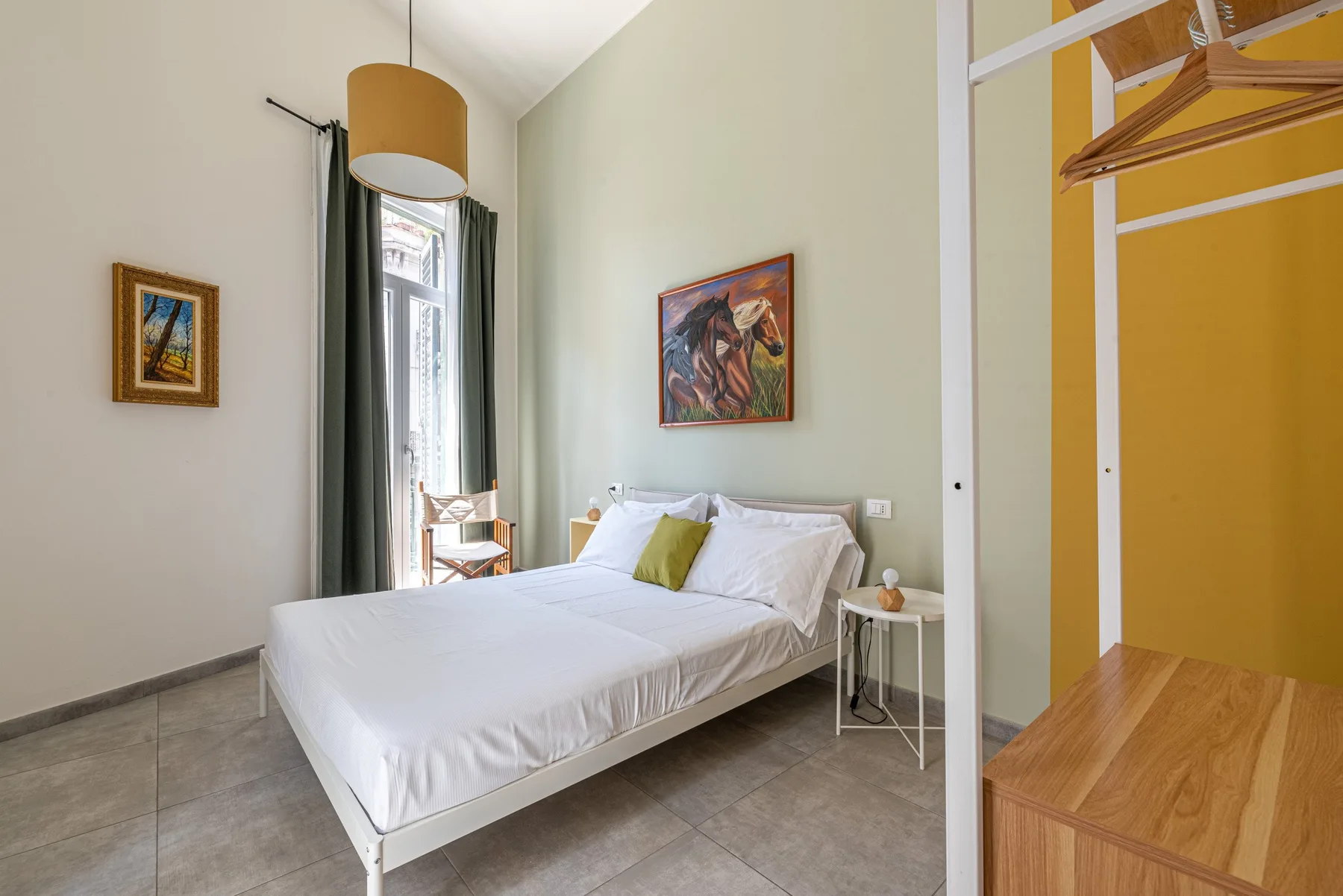 A bedroom with a neatly made bed and artwork on the walls.