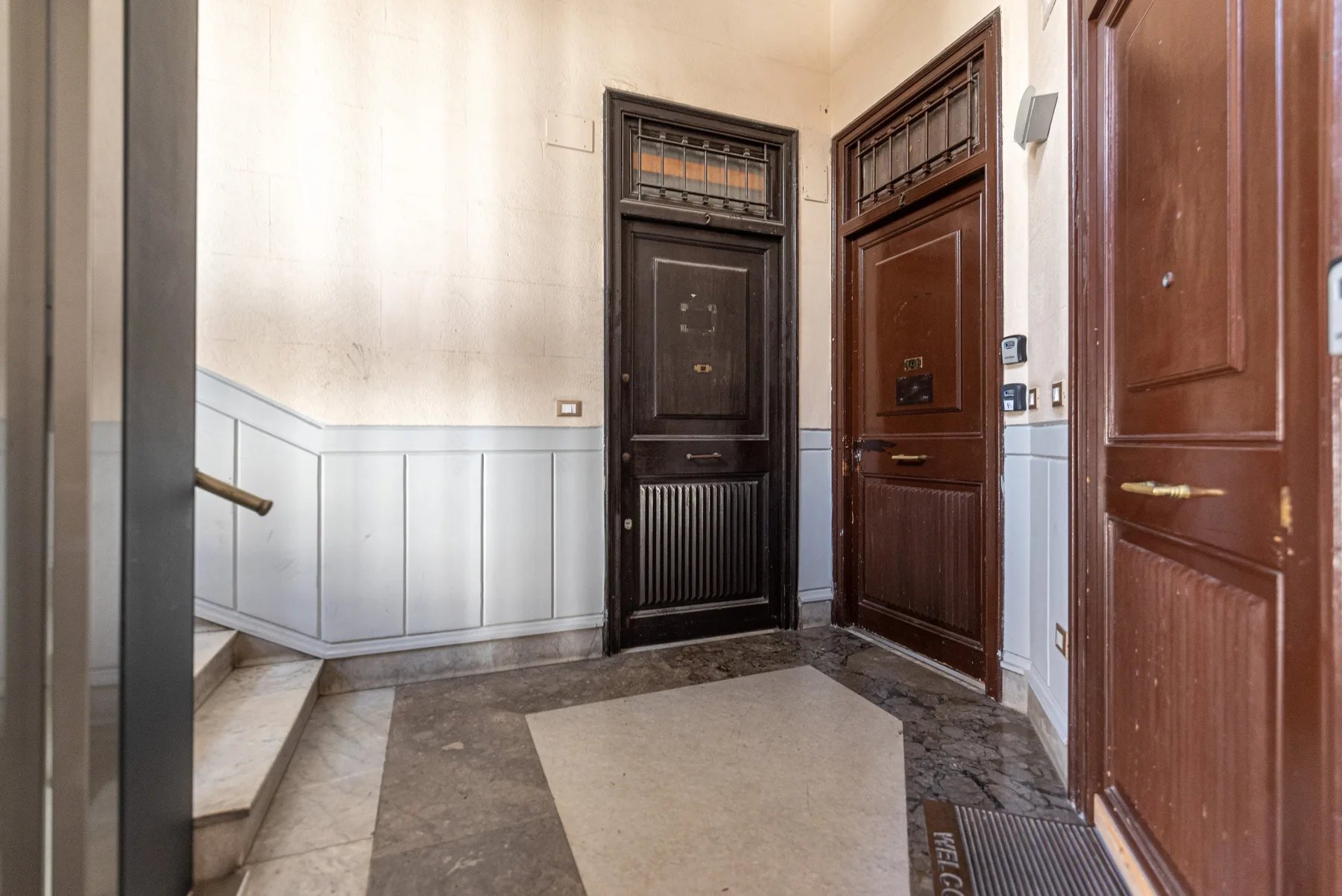 An indoor entry hall with several dark wooden doors and a staircase.